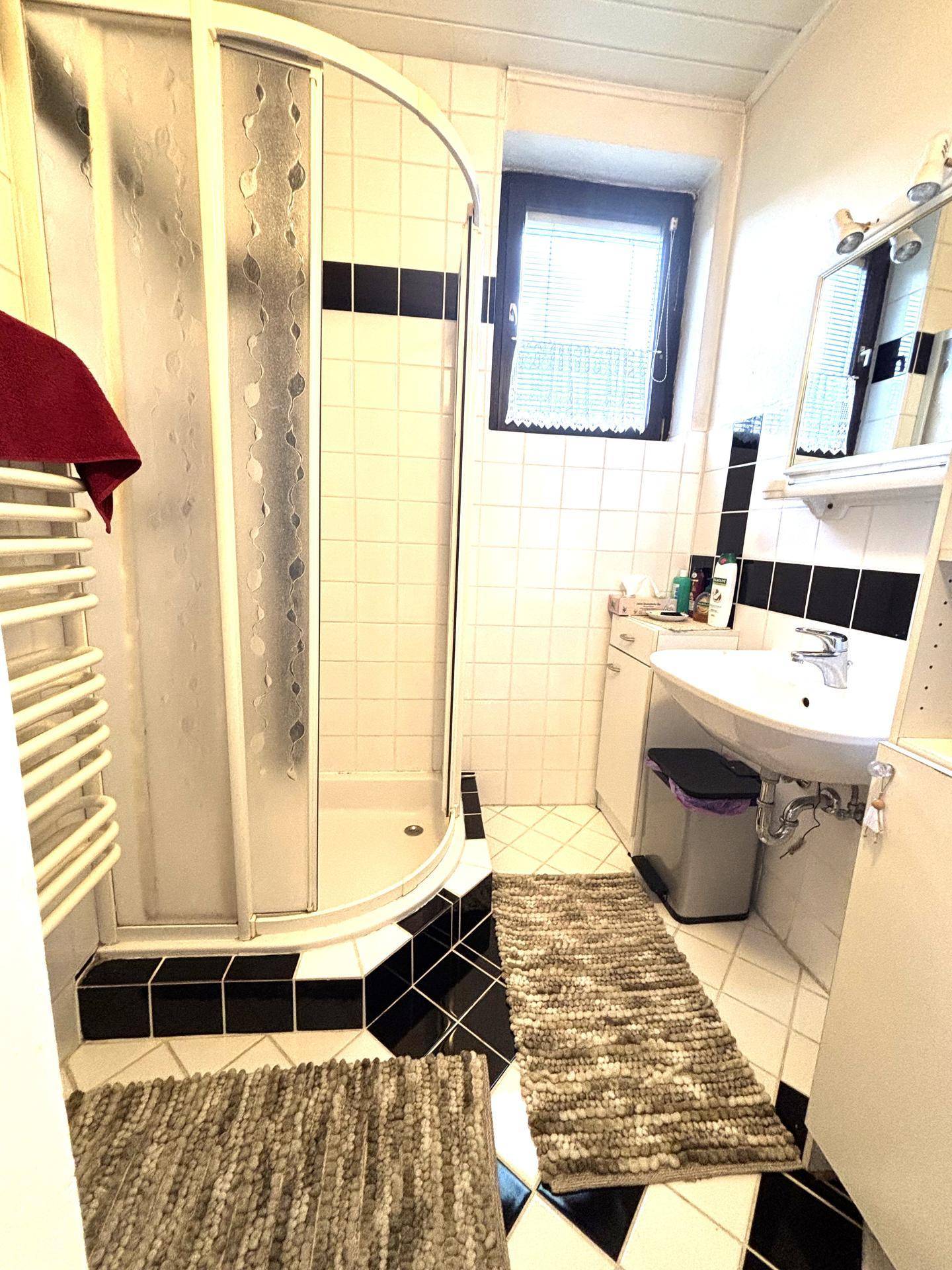 Modernes Badezimmer mit Duschkabine, Waschbecken und schwarz-weißen Fliesen.