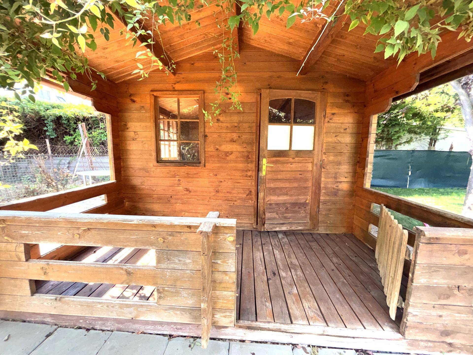 Rustikales Holzhaus mit kleiner Veranda und Holzboden, umgeben von Grün.