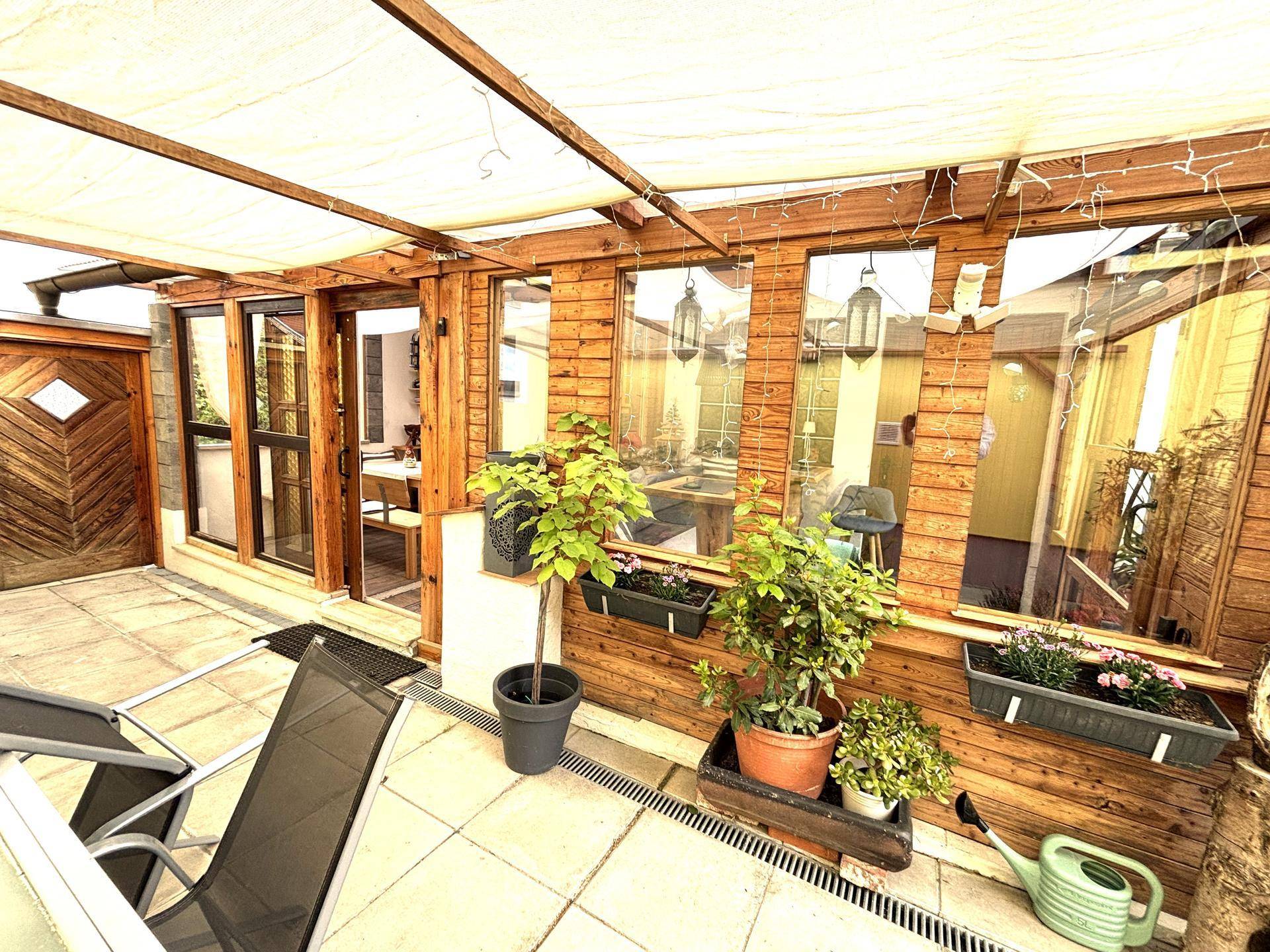 Überdachte Terrasse mit Holzverkleidung, Pflanzen und Sitzgelegenheiten, ideal für entspannte Stunden im Freien.
