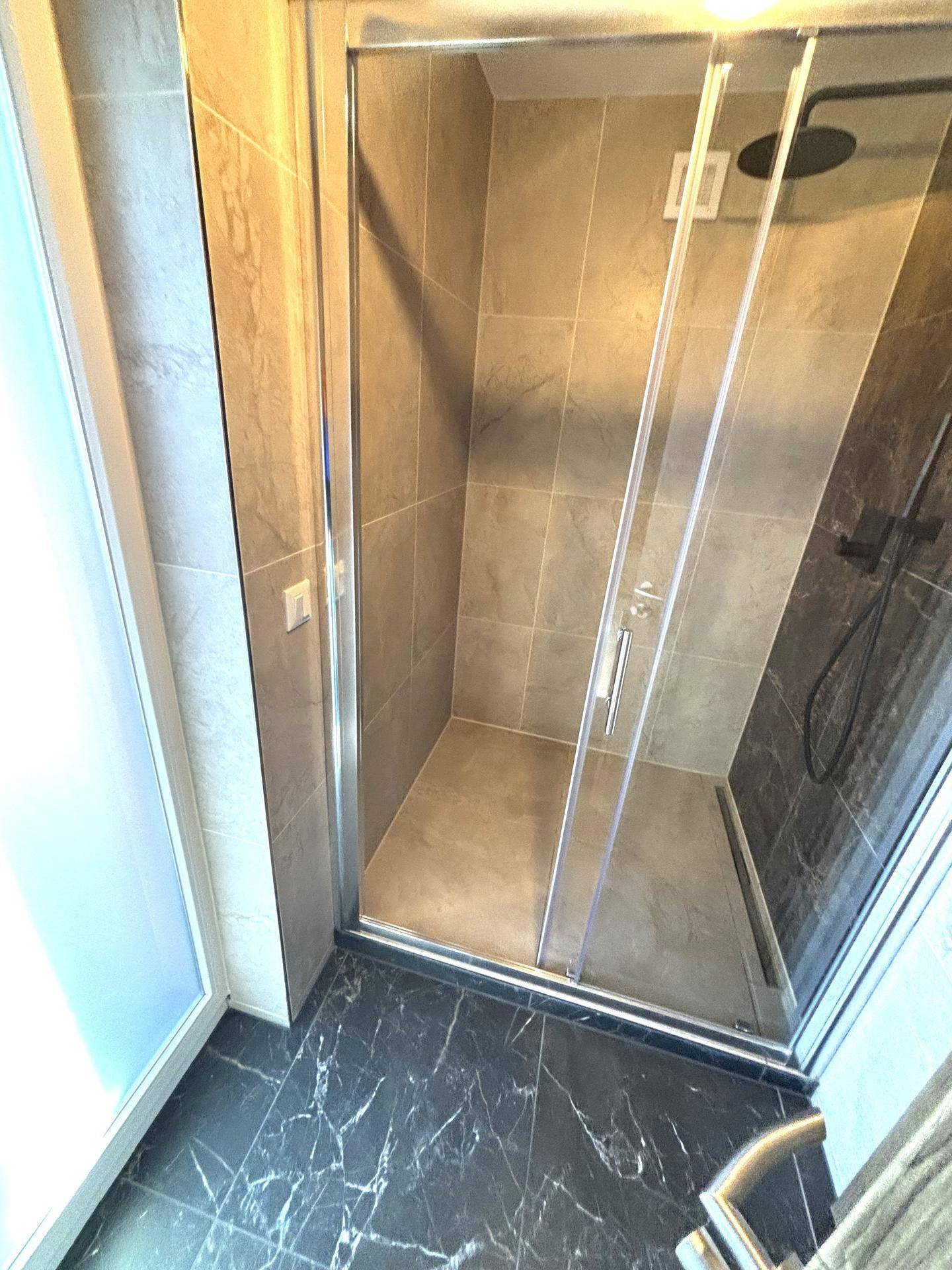 Moderne Duschkabine mit Glaswänden, dunklen Bodenfliesen und beigen Wandfliesen.