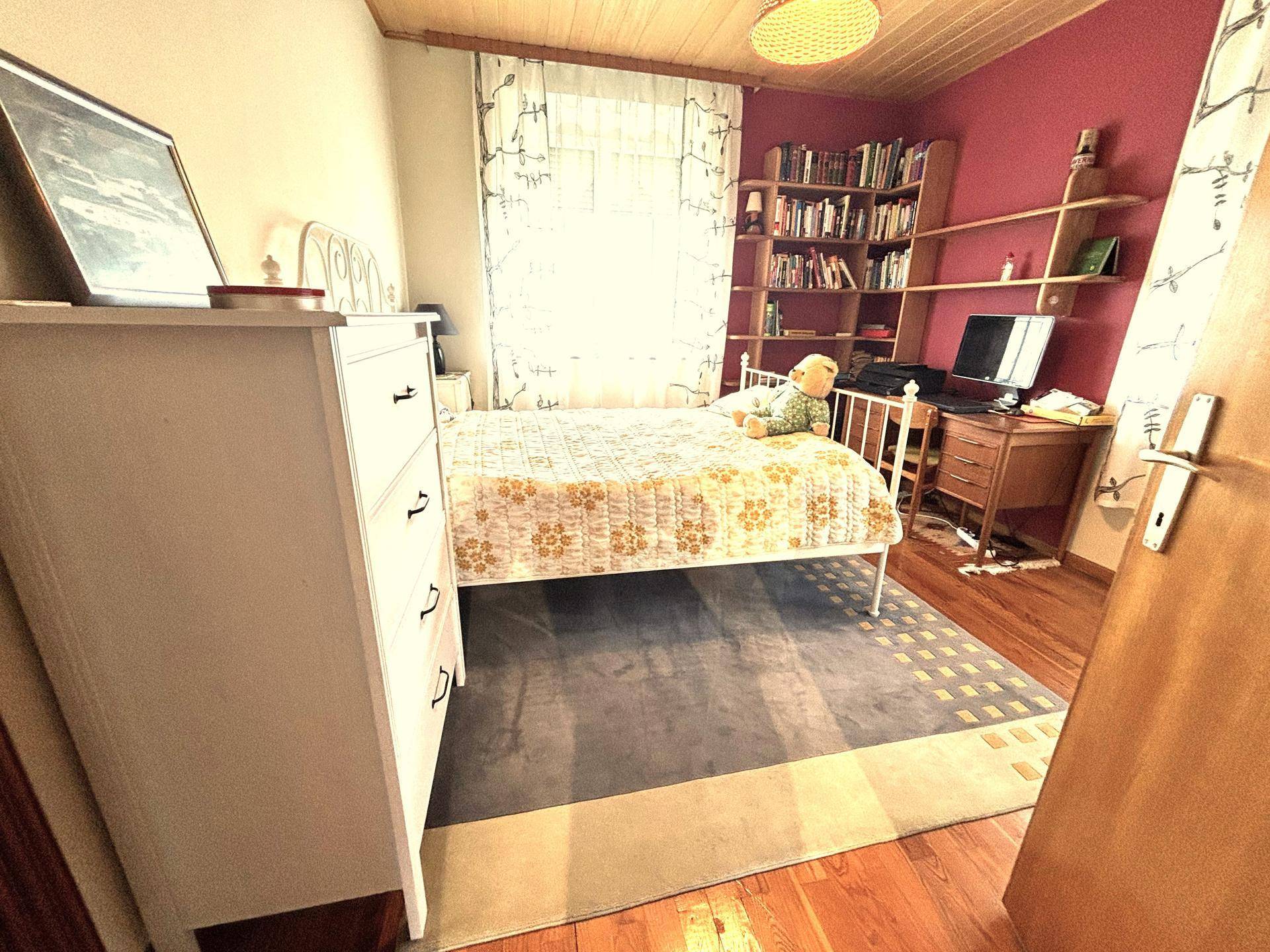 Helles Schlafzimmer mit Holzboden, weißem Bett und Bücherregal.