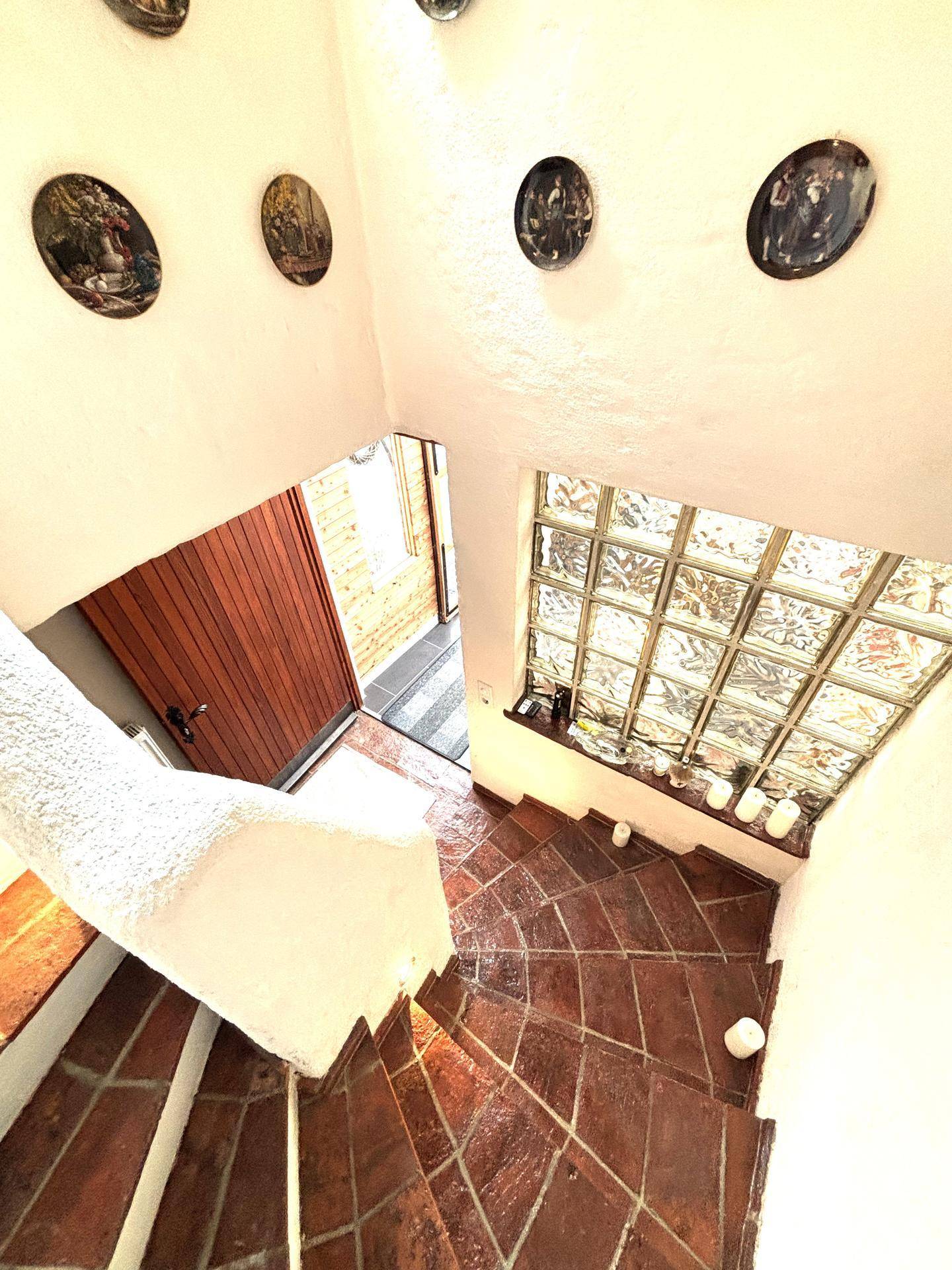 Treppenhaus mit Terrakotta-Fliesen, weiß getünchten Wänden und Glasbaustein-Fenster.