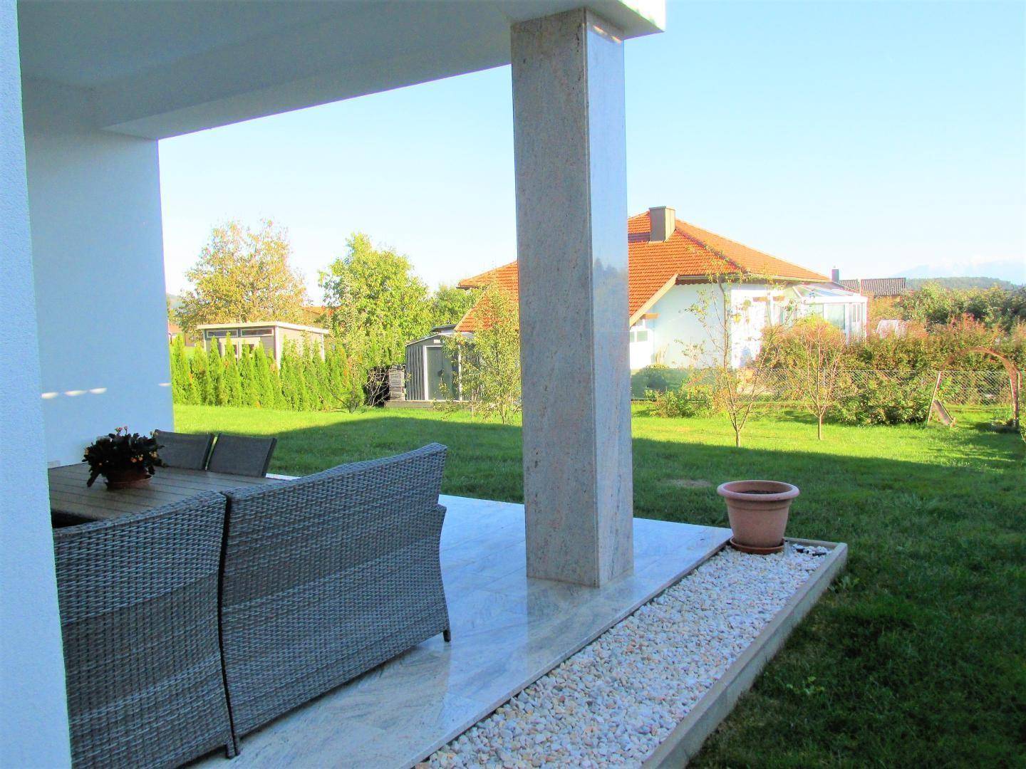 Helle Terrasse mit Rattanmöbeln, Fliesenboden und Blick auf den grünen Gartenbereich.