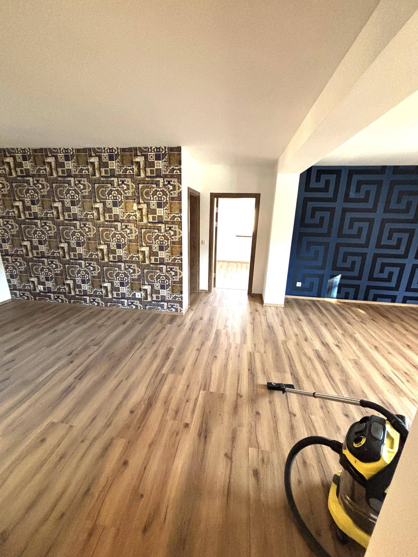 Geräumiges Wohnzimmer mit Laminatboden und zwei auffälligen Akzentwänden in verschiedenen Mustern.