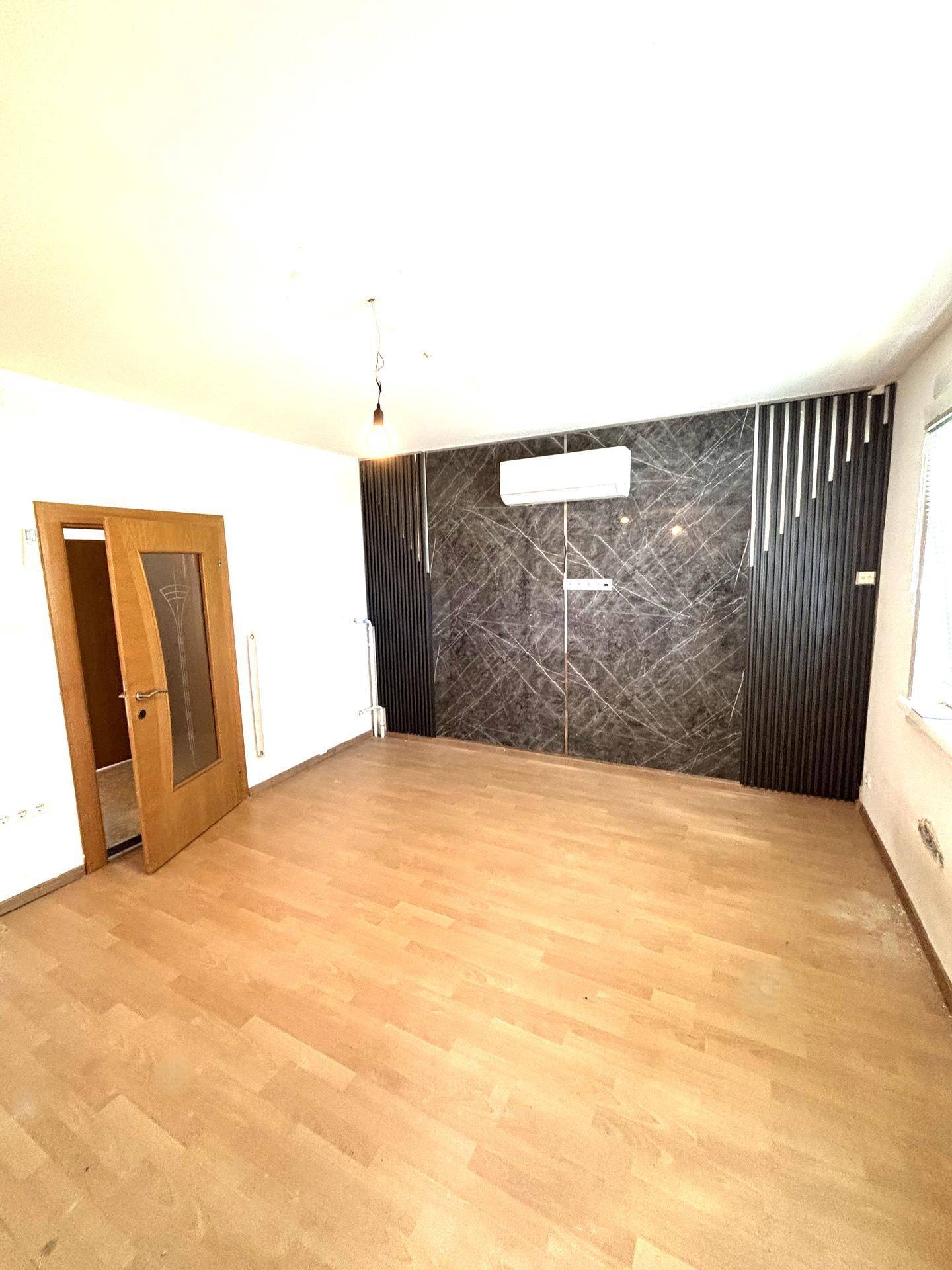Geräumiges Wohnzimmer mit Laminatboden, moderner Wandgestaltung und Klimaanlage.