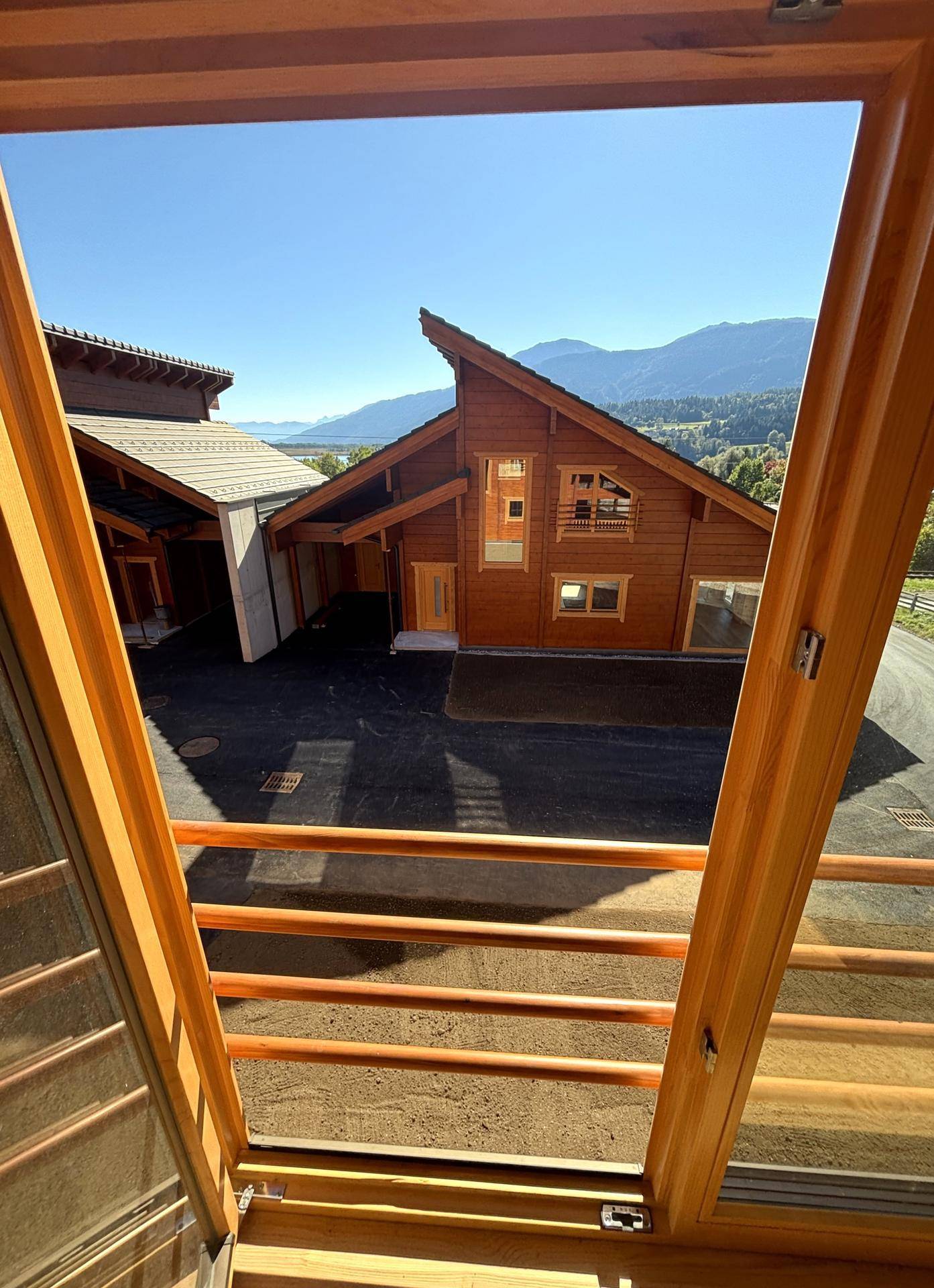 Weitblick vom Fenster auf das Holzhaus, den See und die beeindruckende Bergkulisse.