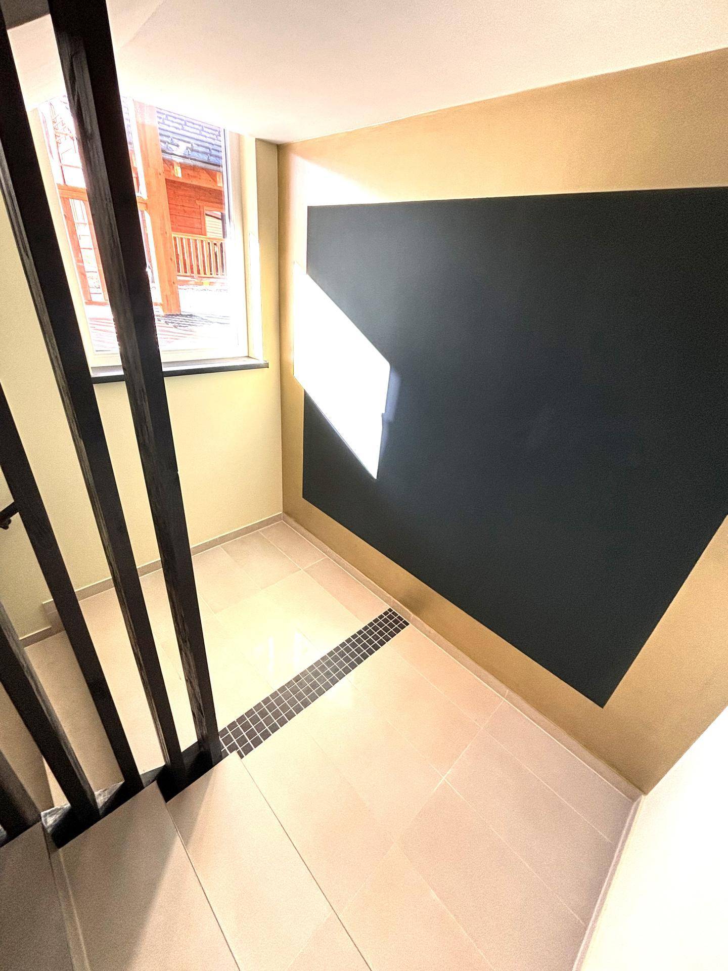 Helles Treppenhaus mit beigen Fliesen und dunklem Geländer, gut beleuchtet durch ein Fenster.