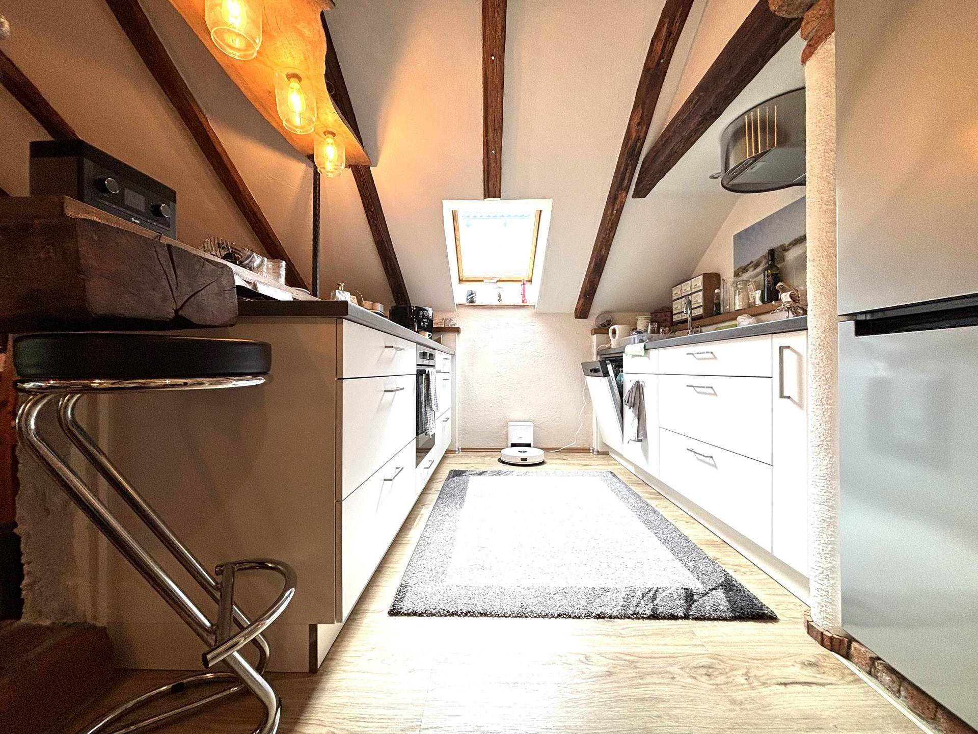 Moderne Küche im Dachgeschoss mit weißen Schränken, Holzboden und Dachfenster.