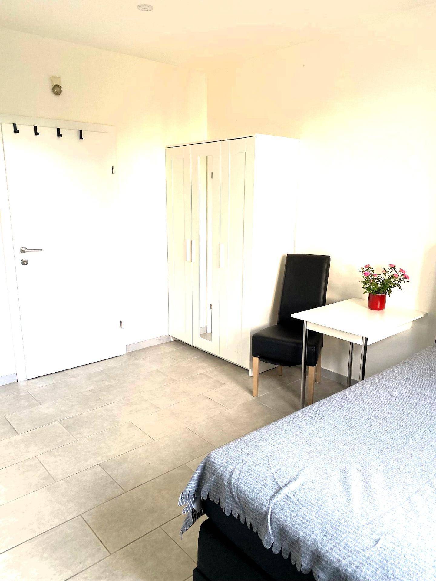Schlafzimmer mit weißem Kleiderschrank, Fliesenboden und einfacher Einrichtung.