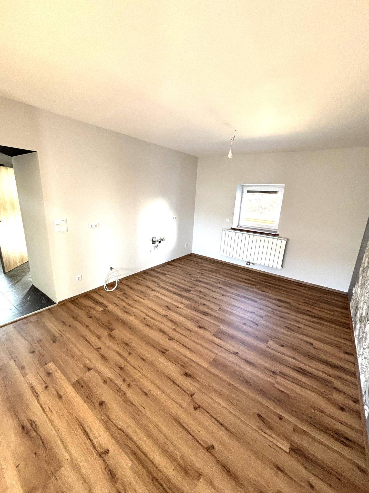 Helles, leeres Zimmer mit Laminatboden und weißen Wänden, bereit zur individuellen Gestaltung.