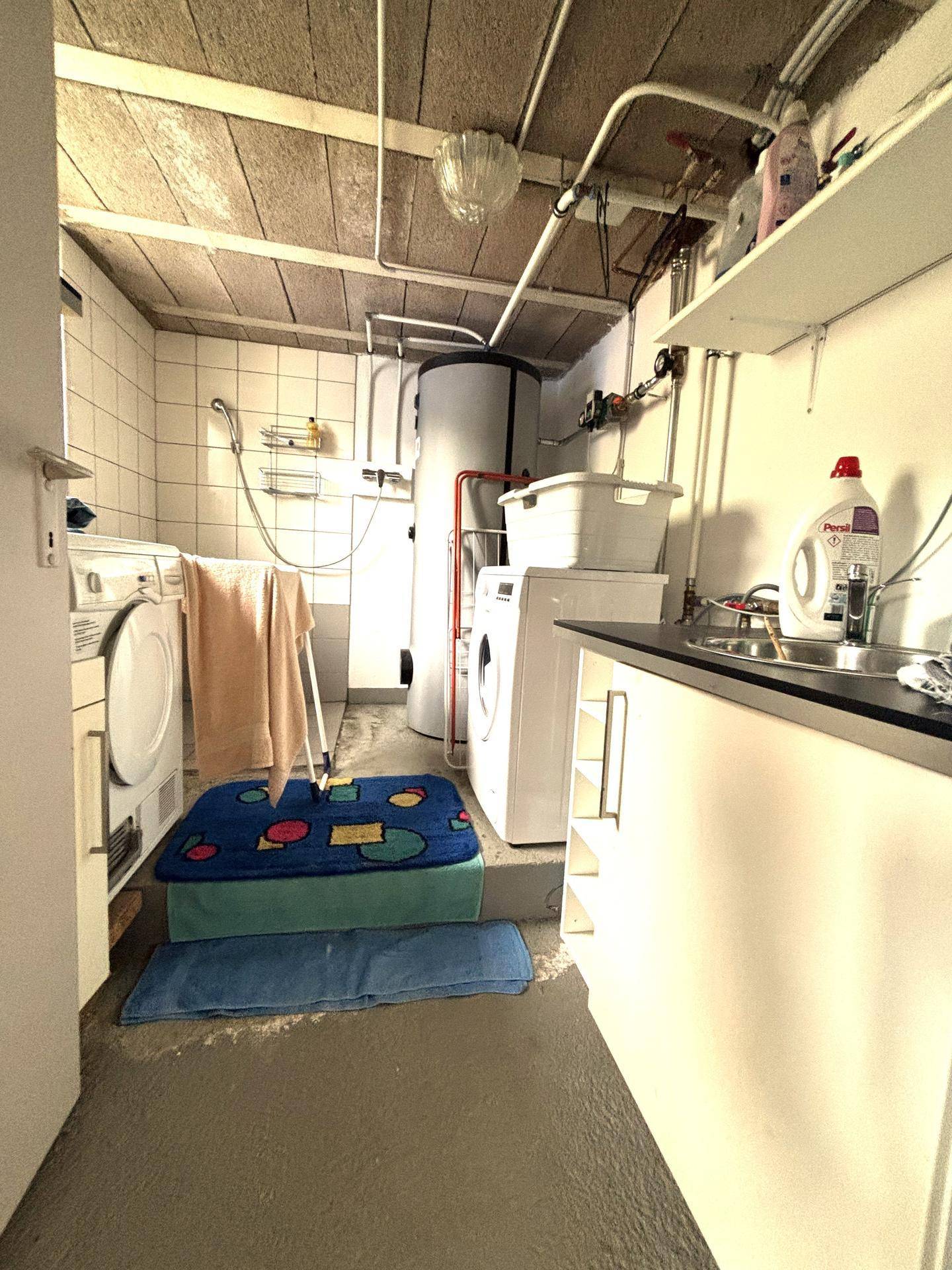 Praktischer Hauswirtschaftsraum mit Waschmaschinen, Trockner und Waschbecken im Kellerbereich.