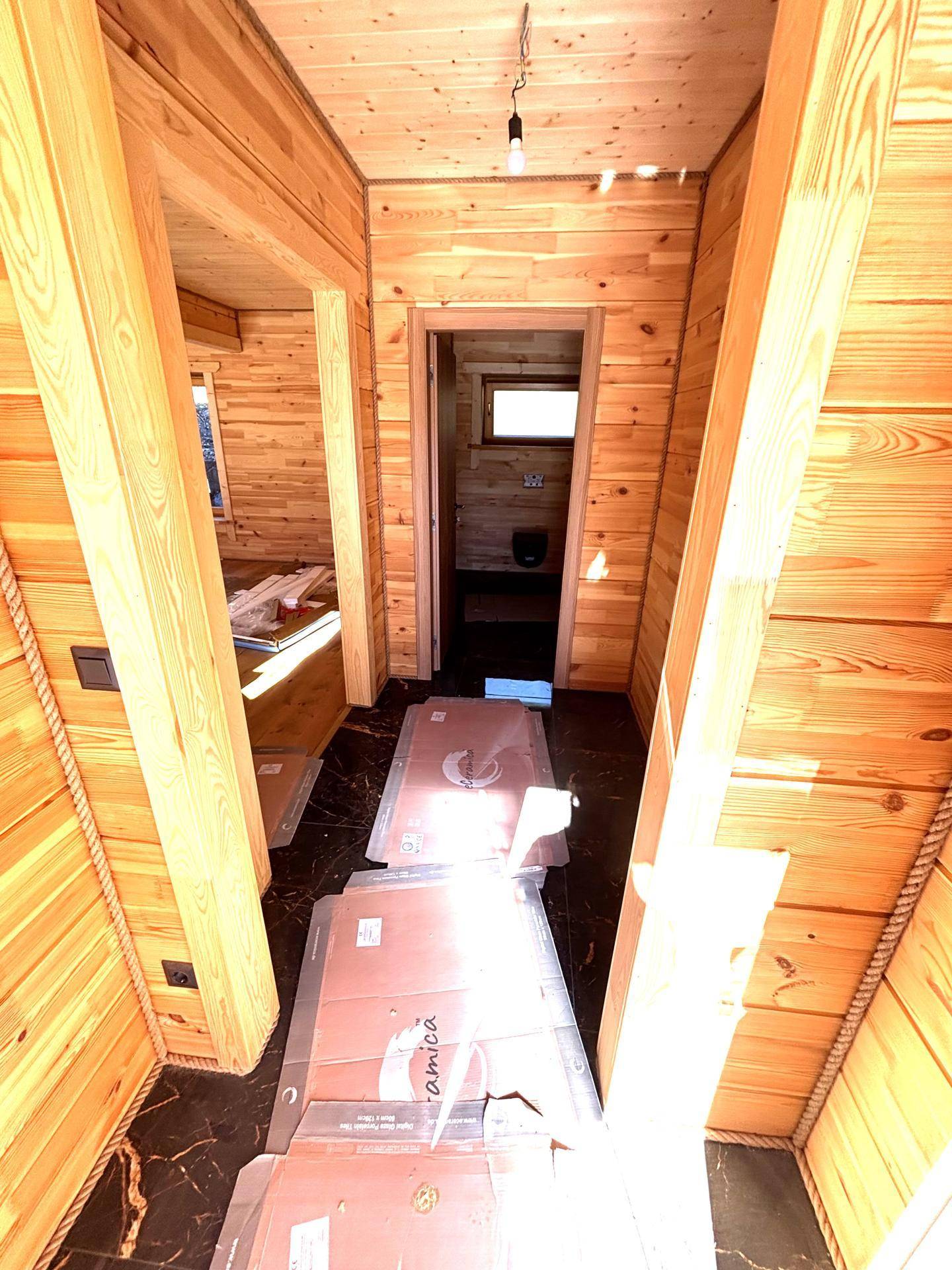 Heller Flur in Holzbauweise mit dunklem Fliesenboden und Blick in ein angrenzendes Badezimmer.