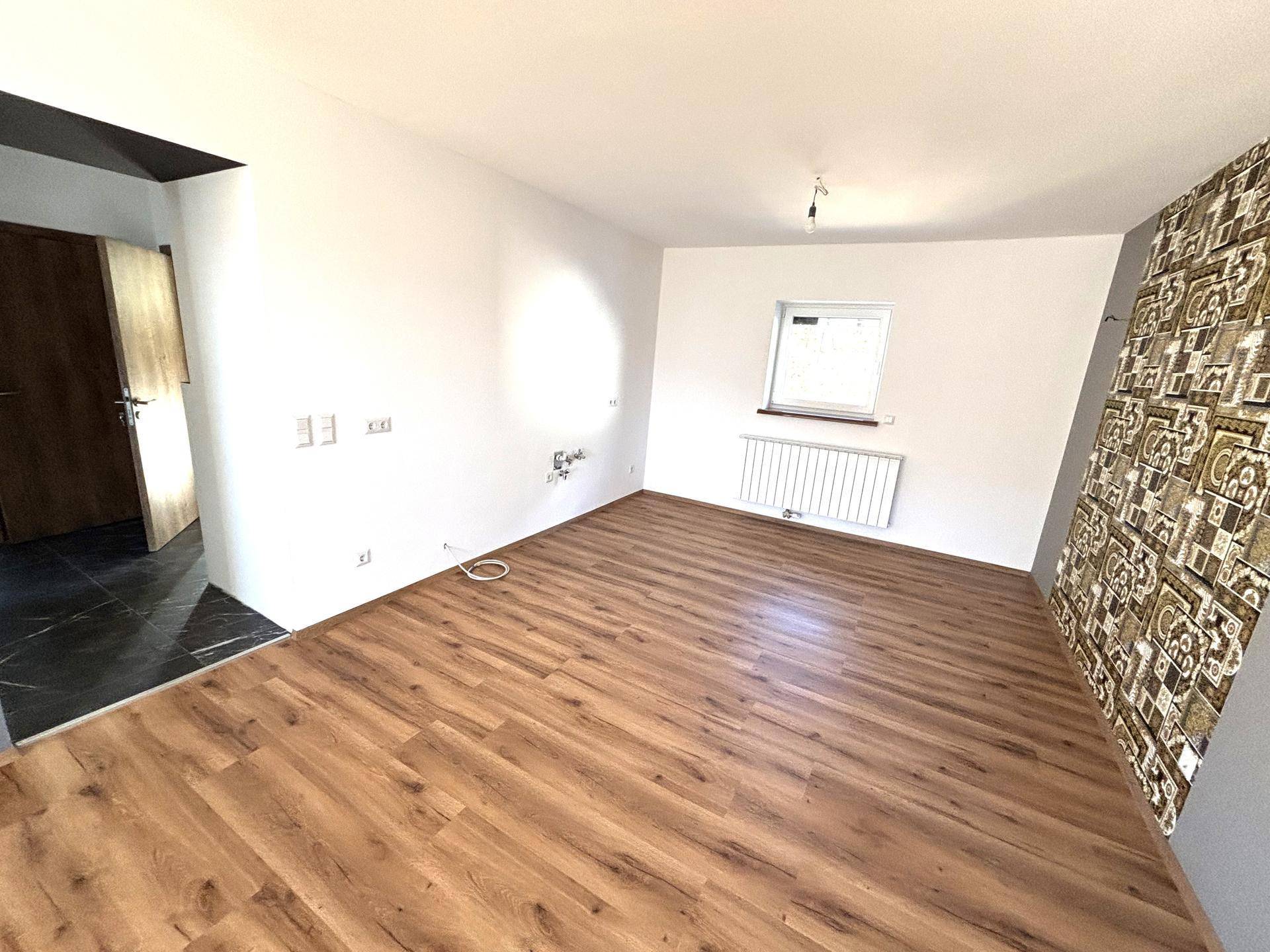 Heller Wohnbereich mit Laminatboden, Heizkörper und einer Akzentwand mit Muster.