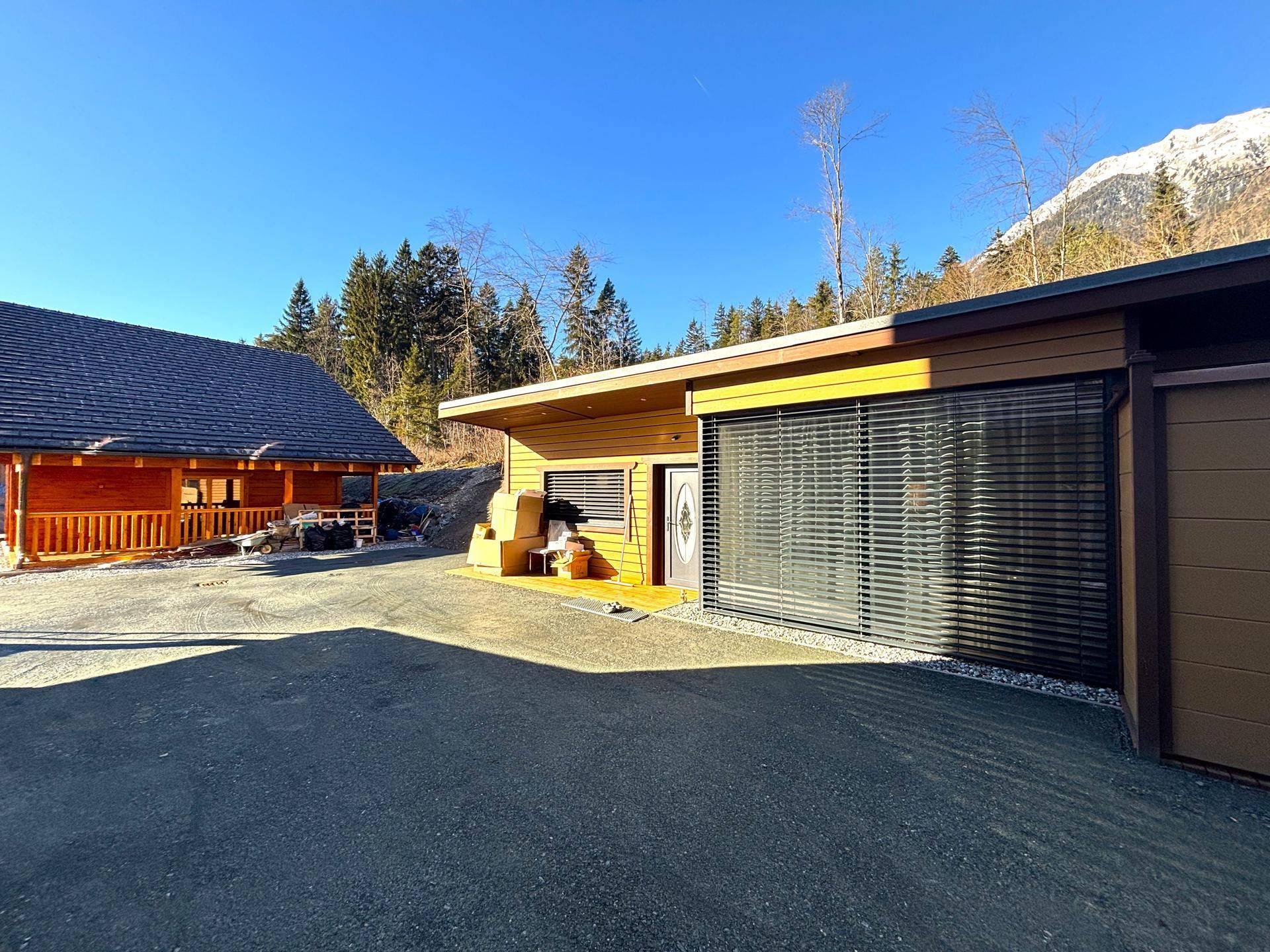 Modernes Gebäude mit Garage und Holzfassade, umgeben von Bäumen unter blauem Himmel.