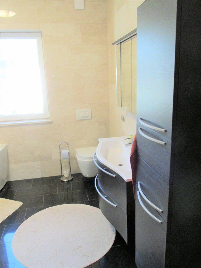 Modernes Badezimmer mit Waschtisch, Spiegel und dunklem Fliesenboden.