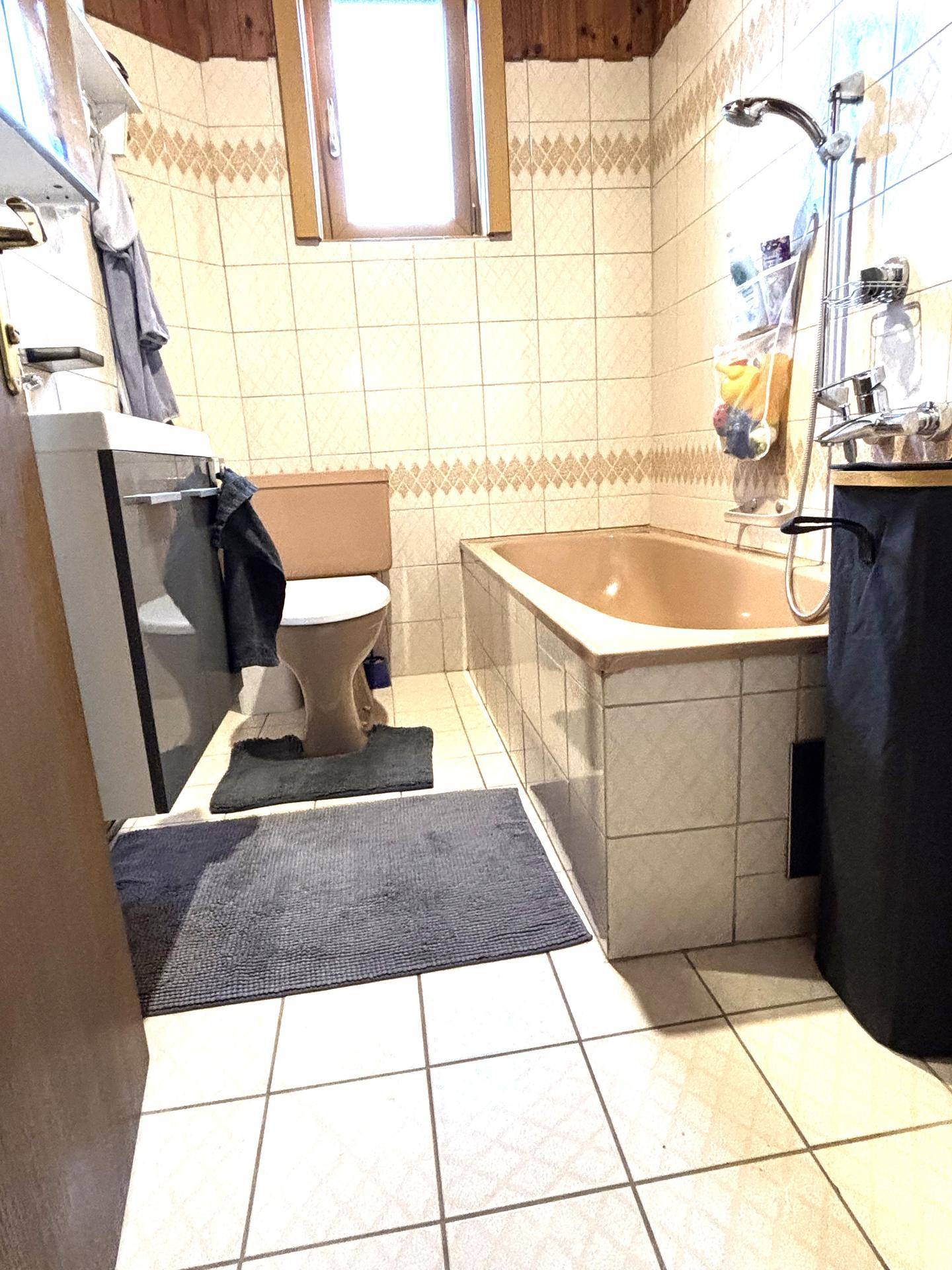 Badezimmer mit Badewanne, WC und Fliesen an Wänden und Boden in einem älteren Stil.