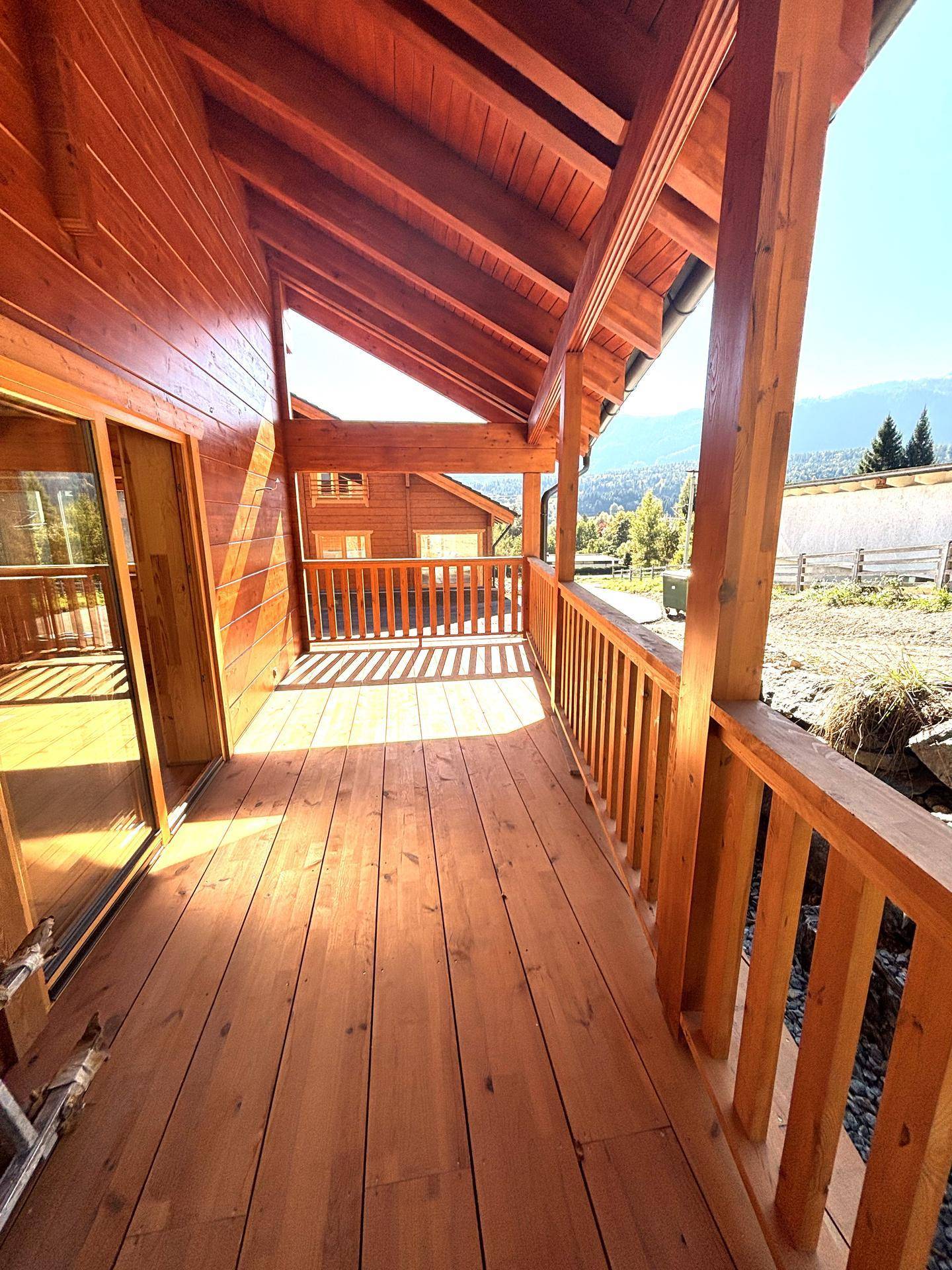 Überdachter Holzbalkon mit Geländer und Blick auf die umliegende grüne Landschaft.