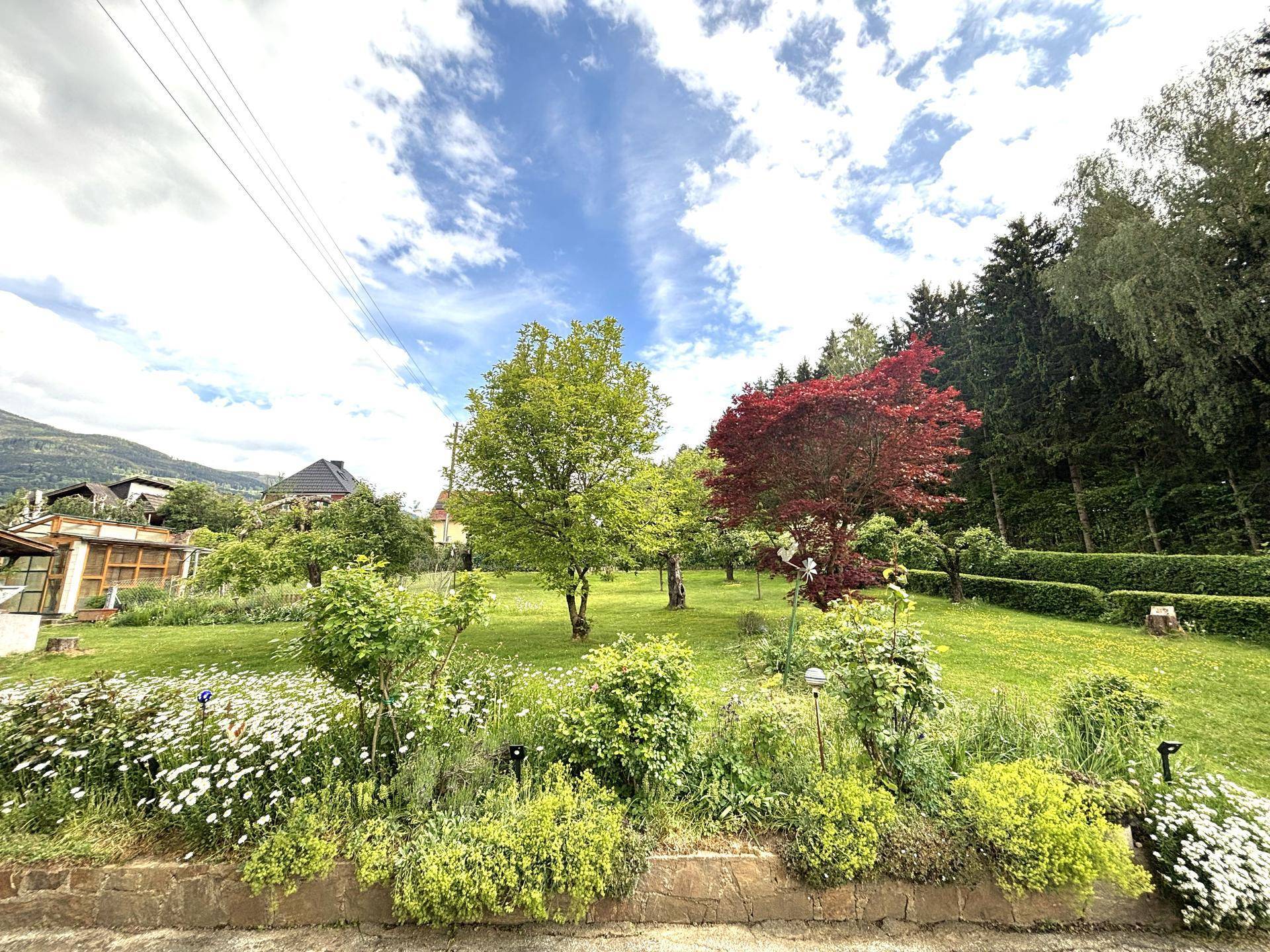 Blühender Garten mit verschiedenen Pflanzen, Bäumen und weitem Blick in die Landschaft.