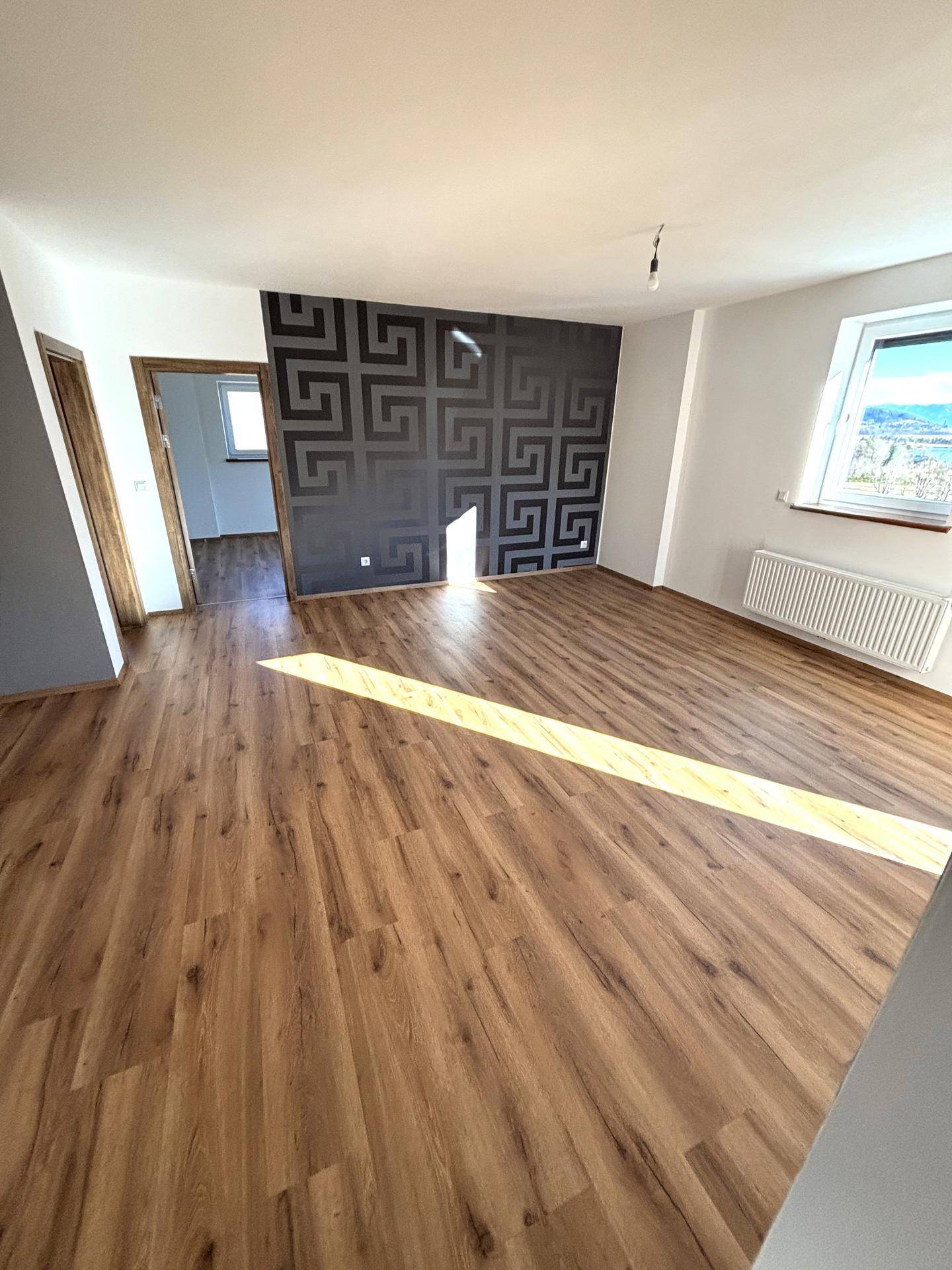 Heller Wohnbereich mit Laminatboden, Heizkörper und einer Akzentwand mit Muster.