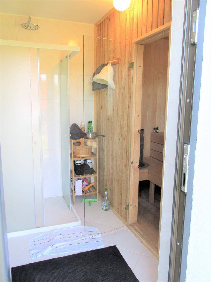 Badezimmer mit Duschbereich und angrenzender Holzsauna für Wellnessmomente.