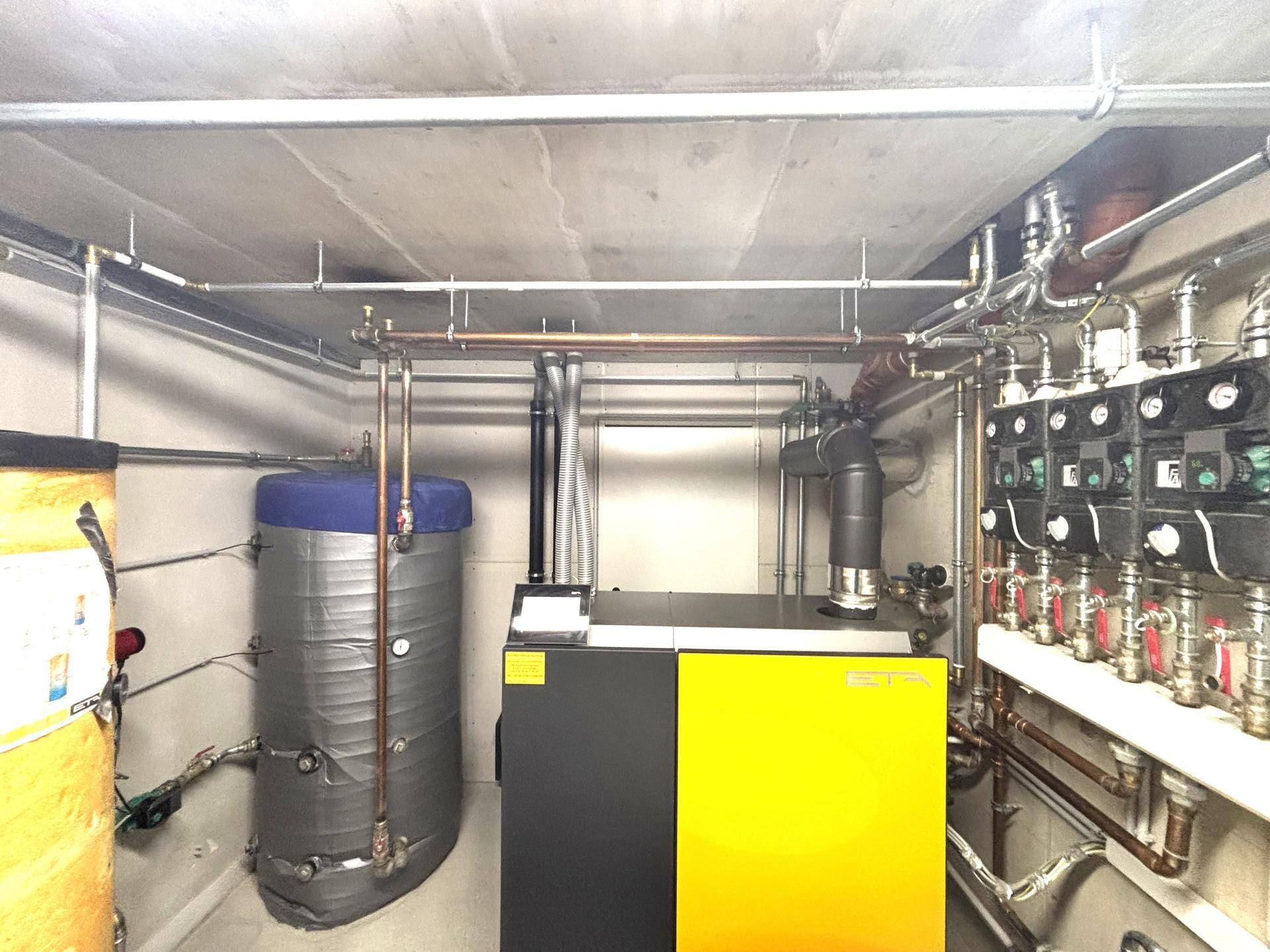 Heizungsraum mit moderner Heizungsanlage, Warmwasserspeicher und sichtbaren Rohrleitungen.