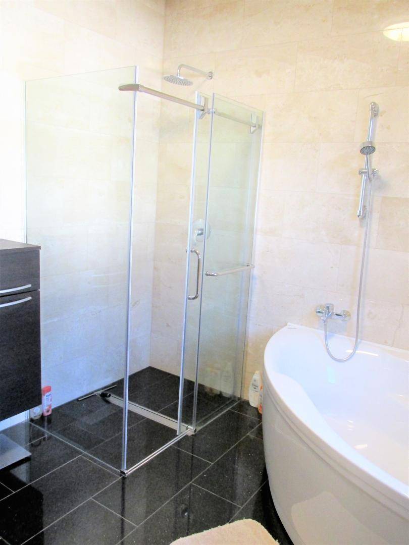 Helles Badezimmer mit moderner Glasdusche und Duschkopf, neben einer Eckbadewanne.