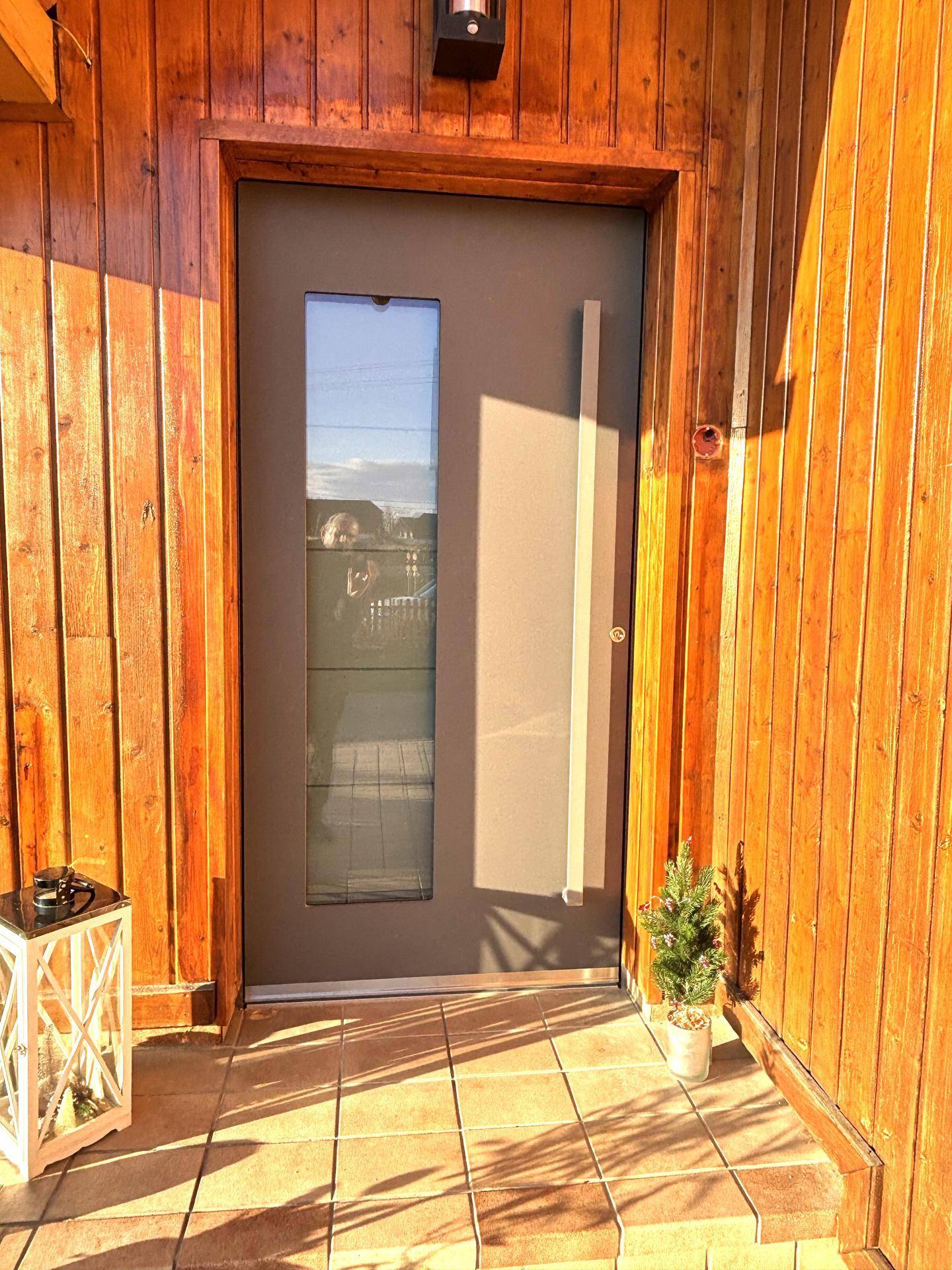 Moderner Hauseingang mit Holzwandverkleidung, großer Glastür und Fliesenboden im Eingangsbereich.