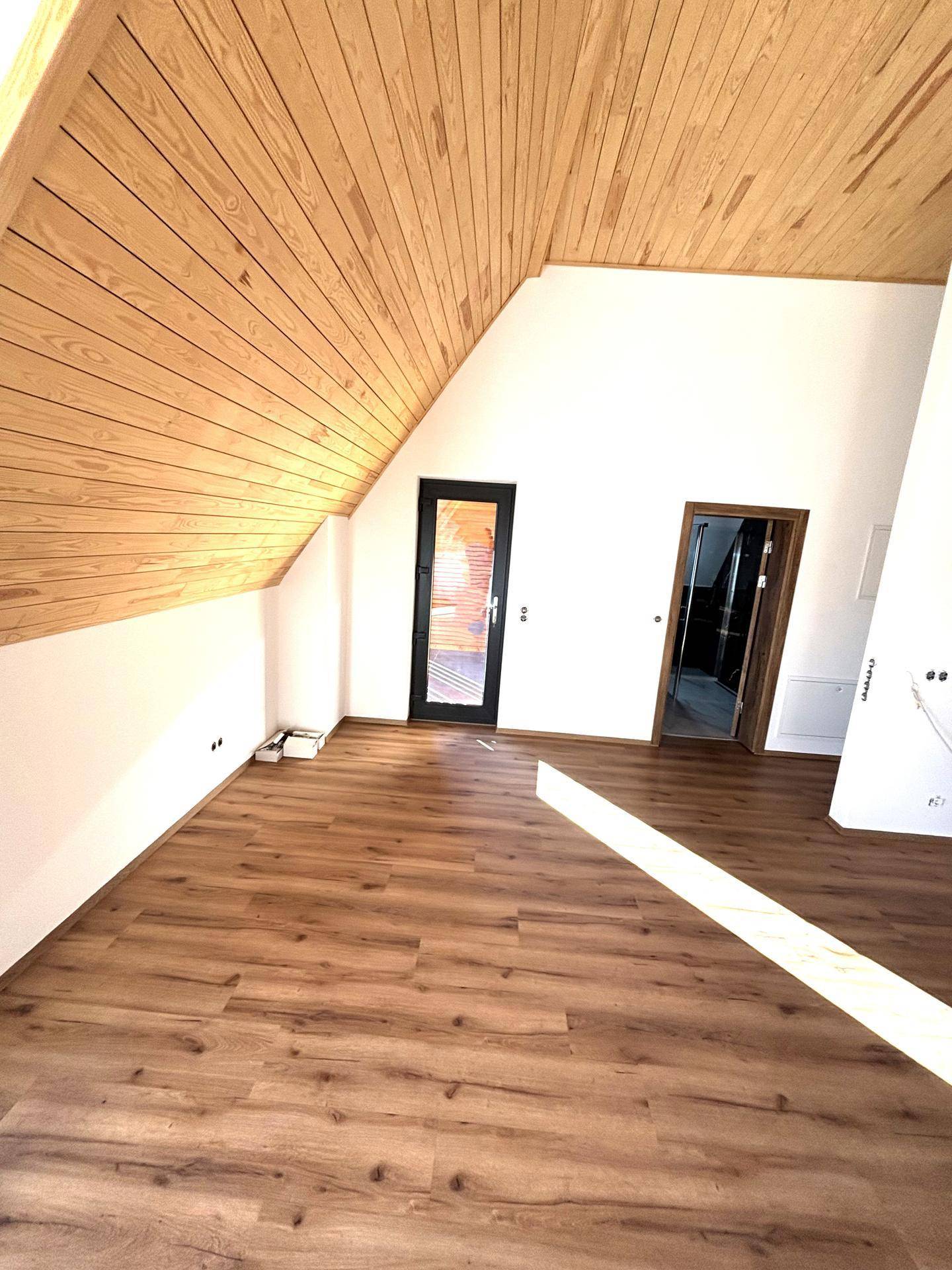 Geräumiger Wohnbereich mit Holzdachschrägen, Laminatboden und Zugang zu weiteren Räumen.