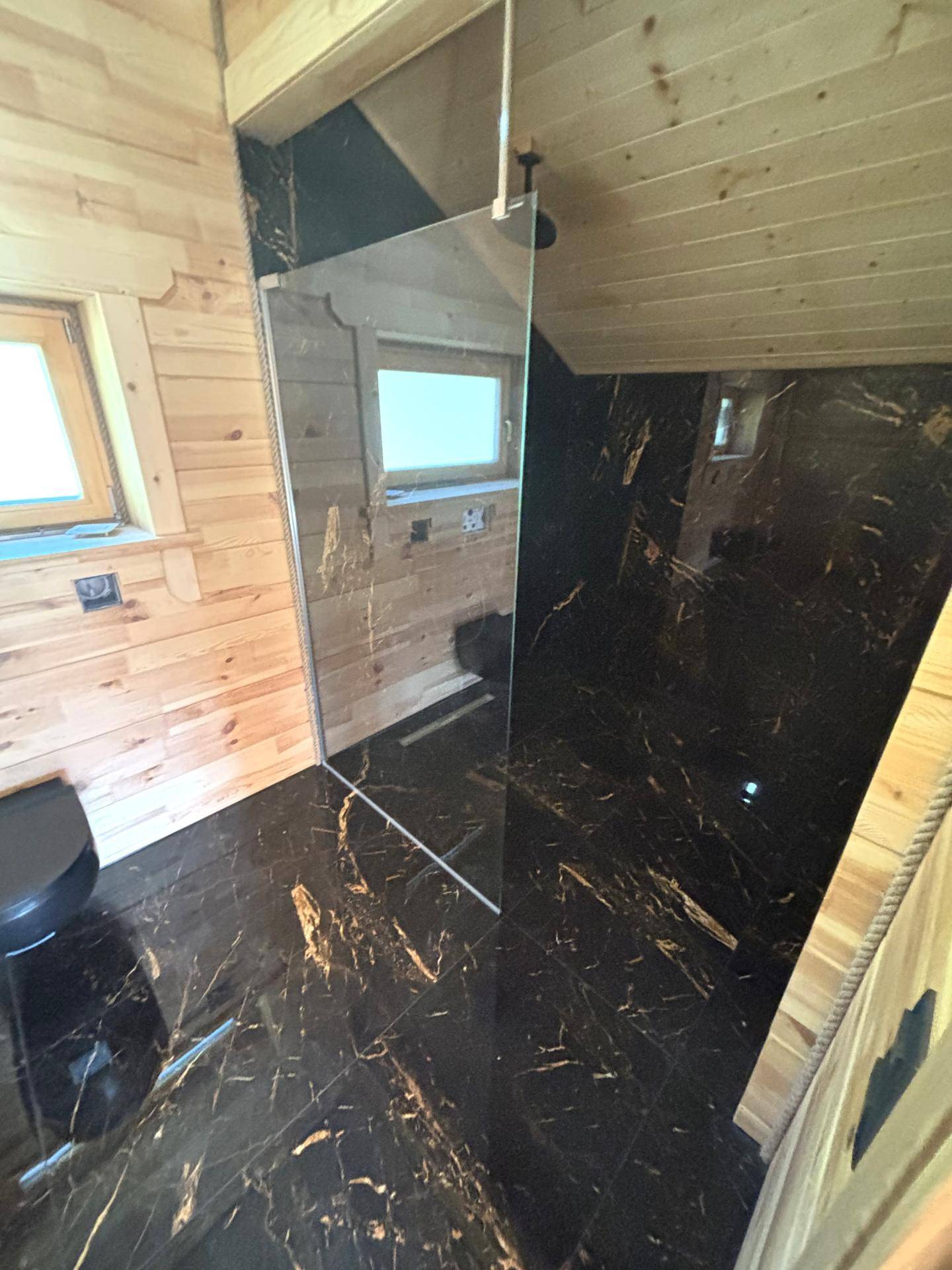 Modernes Badezimmer mit dunklen Marmorfliesen, Holzvertäfelung und begehbarer Dusche.