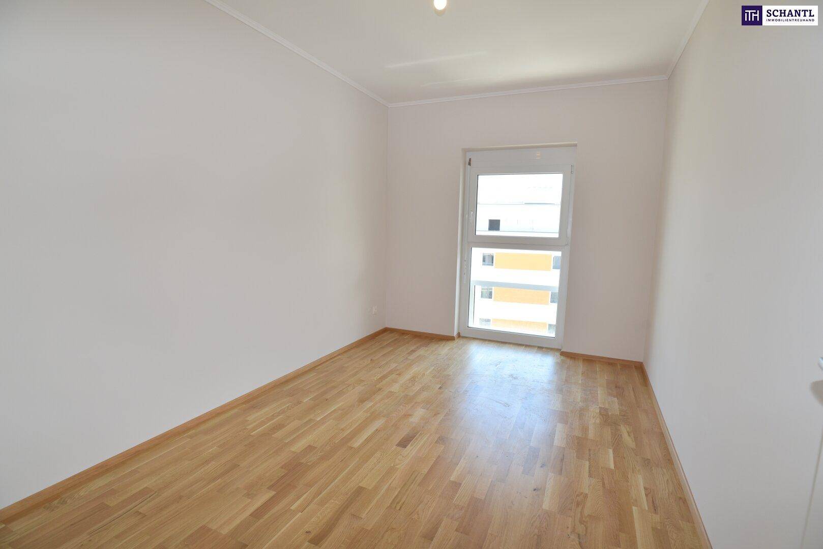 Helles Schlafzimmer mit Parkettboden und großem Fenster in einem Neubau, gut beleuchtet.