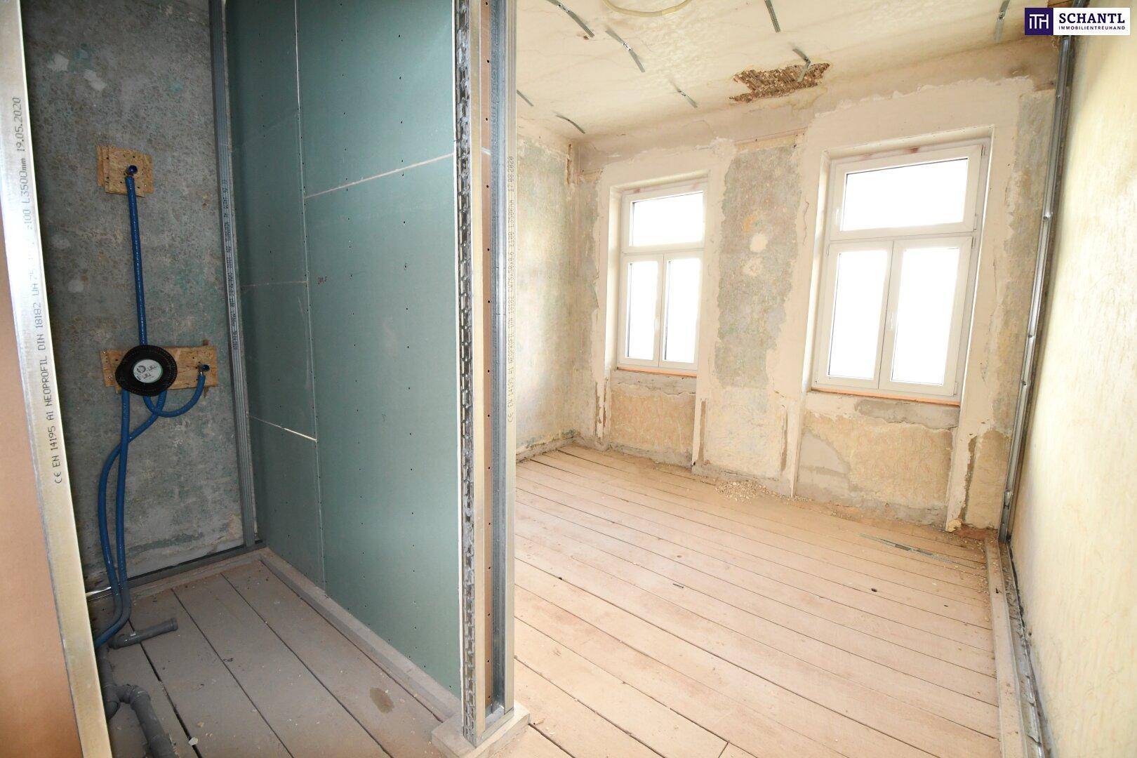 Raum im Rohbauzustand mit freigelegten Wänden, Holzdielenboden und vorbereiteten Sanitäranschlüssen.
