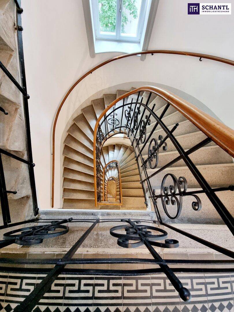Elegantes Treppenhaus mit geschwungener Steintreppe, schmiedeeisernem Geländer und Oberlicht.