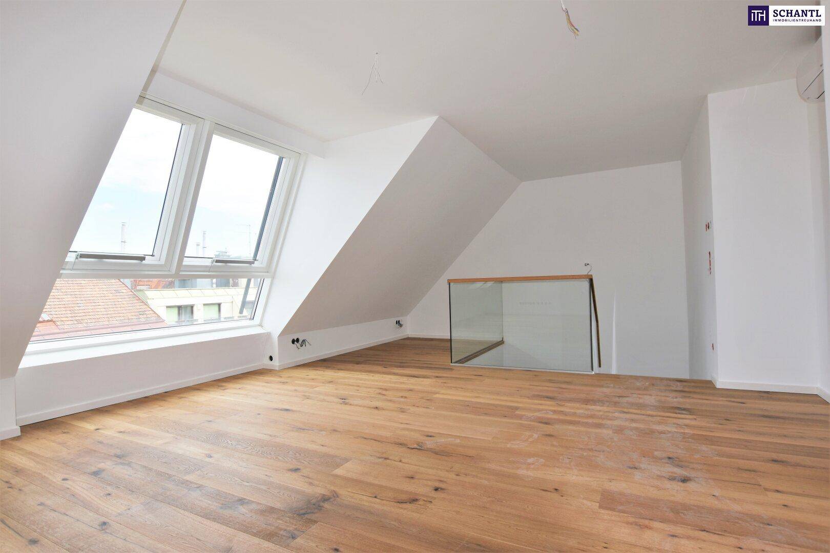 Geräumiger Dachgeschossraum mit Holzboden, Dachschrägen und großen Fenstern, noch im Ausbau.