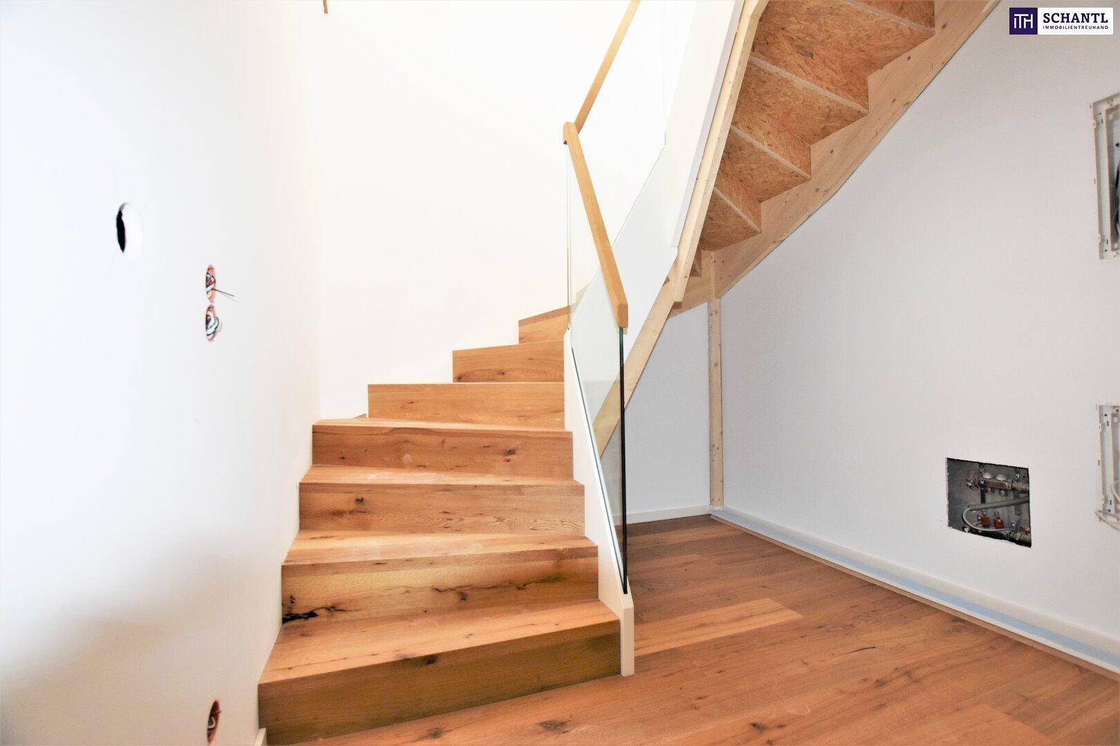 Moderne Holztreppe mit Glasgeländer in einem noch unfertigen Innenbereich.
