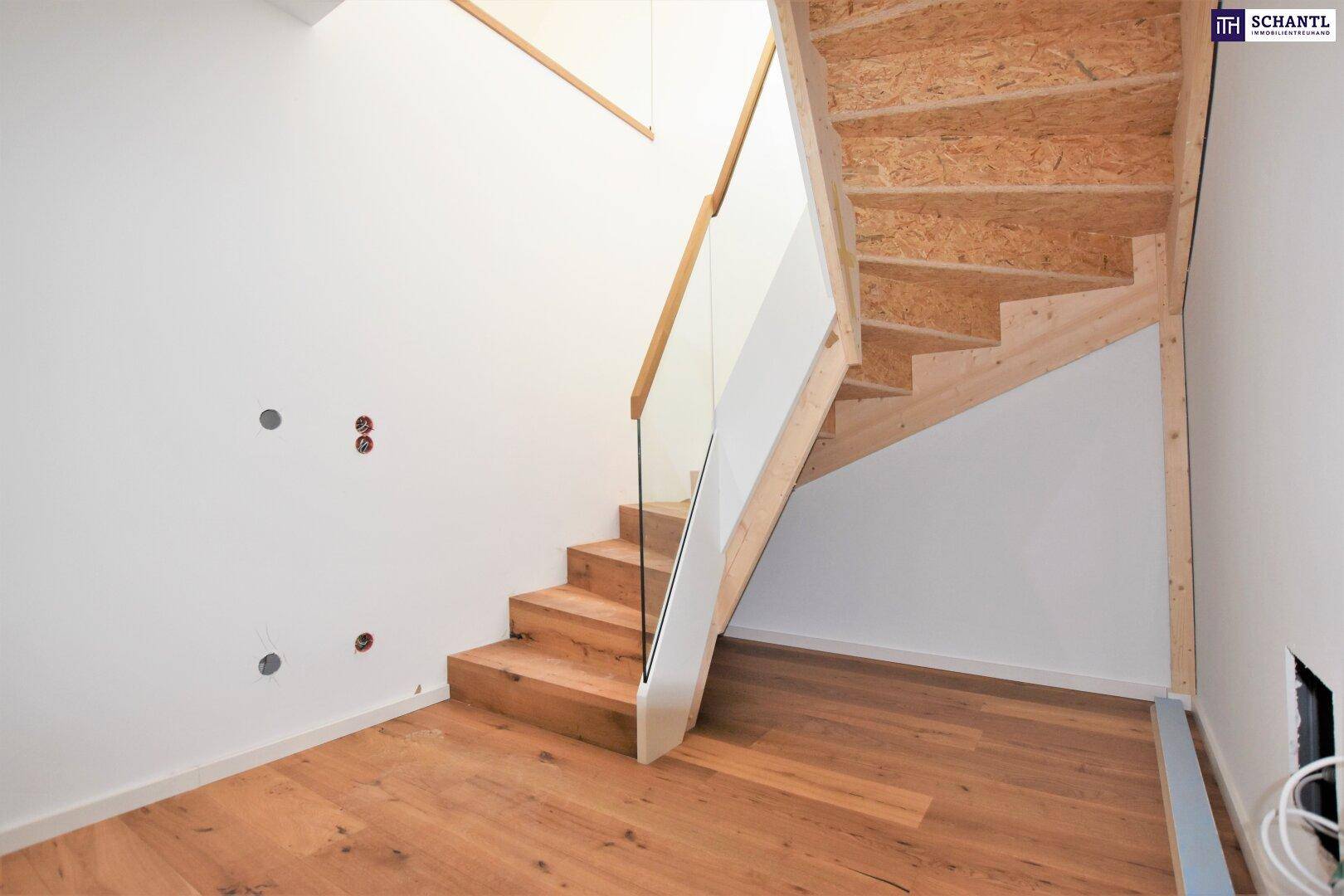 Moderne Holztreppe mit Glasgeländer in einem hellen, noch unfertigen Treppenhaus.