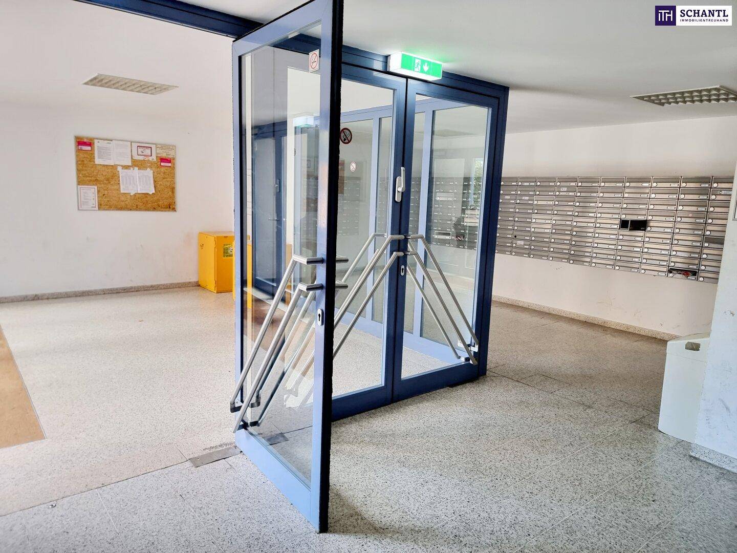 Eingangsbereich eines Gebäudes mit Glasportal, Briefkästen und einer Rampe für Barrierefreiheit.