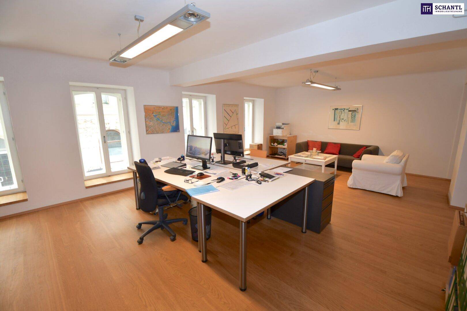 Geräumiges Büro mit mehreren Arbeitsplätzen, Sitzbereich und großen Fenstern für viel Tageslicht.