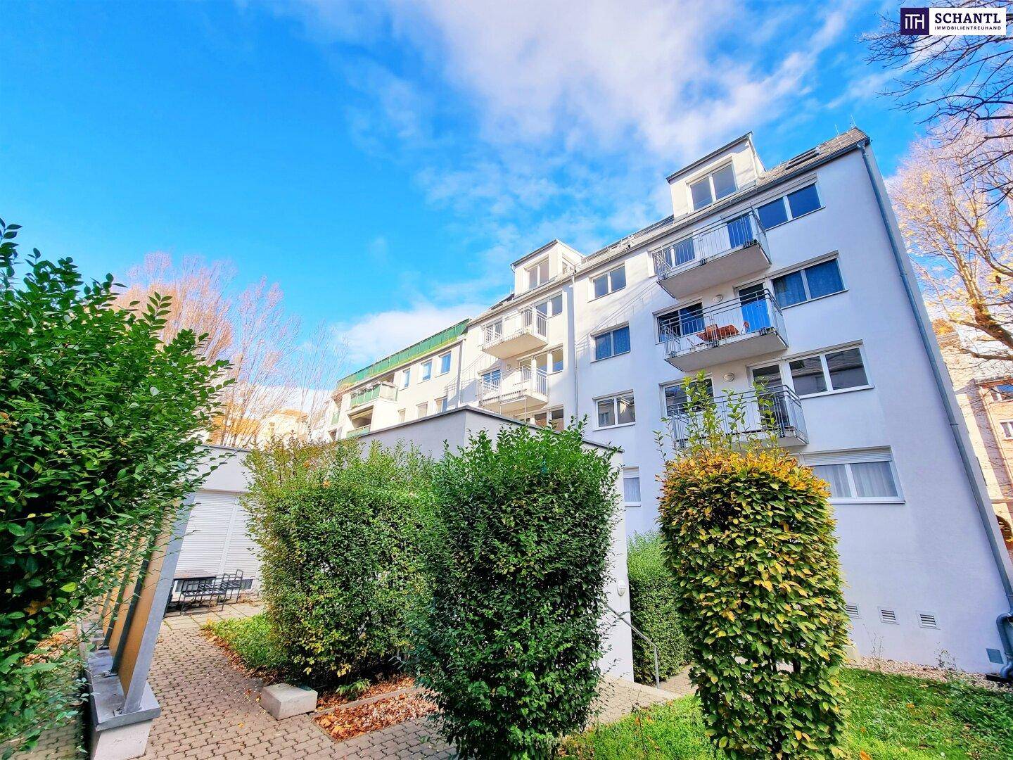 Modernes Mehrfamilienhaus mit weißer Fassade, Balkonen und gepflegter Grünanlage unter blauem Himmel.