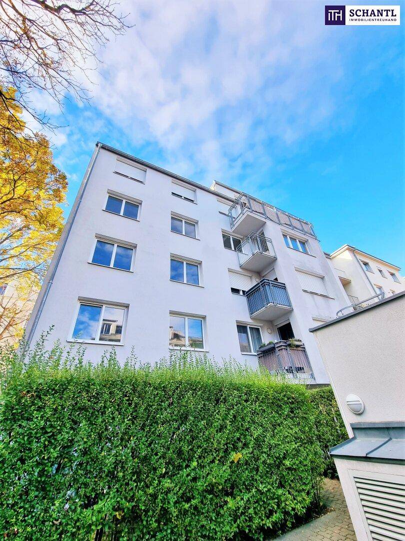 Mehrstöckiges Wohngebäude mit Balkonen und einer gepflegten Hecke im Vordergrund unter blauem Himmel.