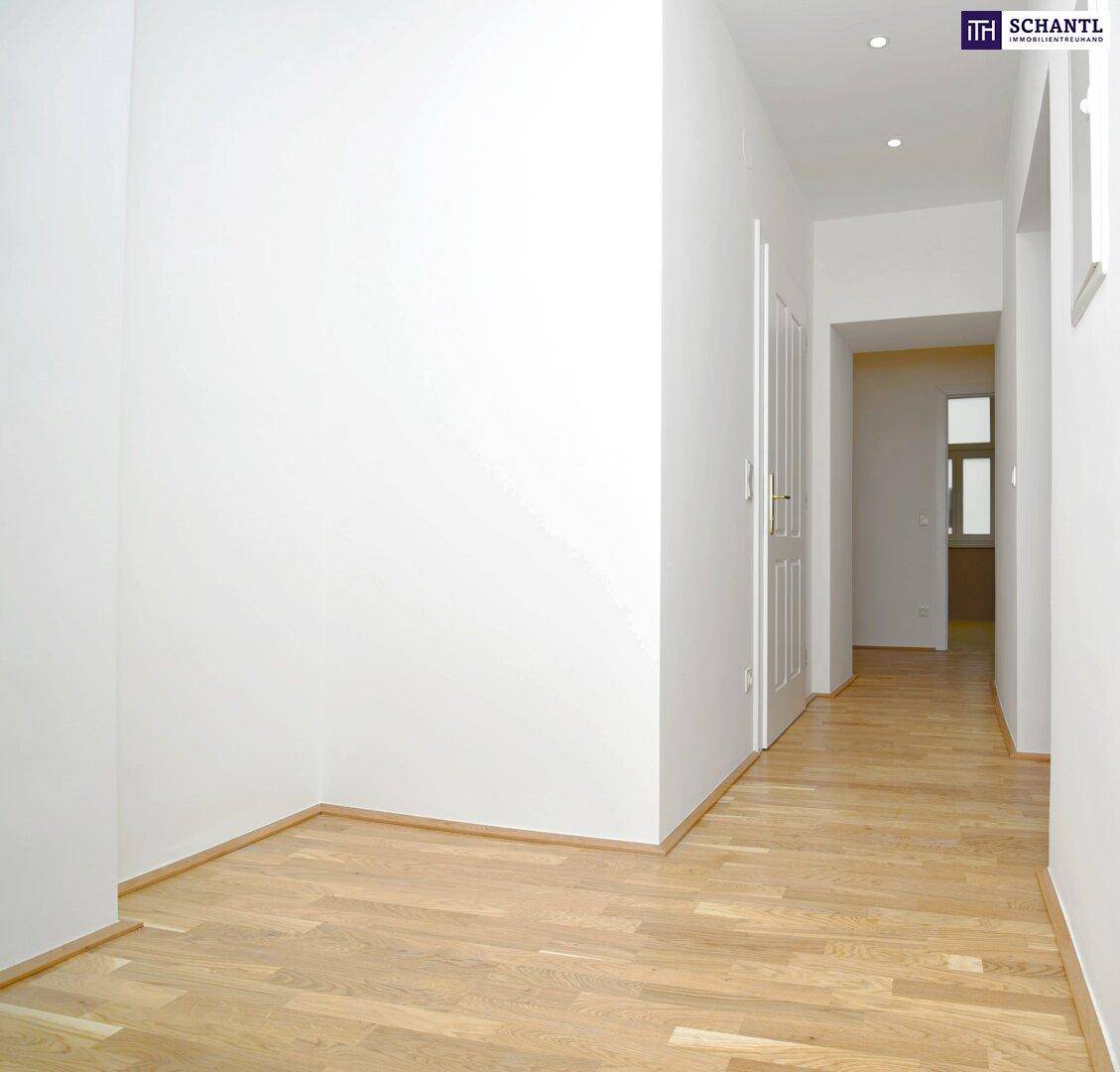 Heller Flur mit Holzboden und weißen Wänden, der zu weiteren Räumen führt.