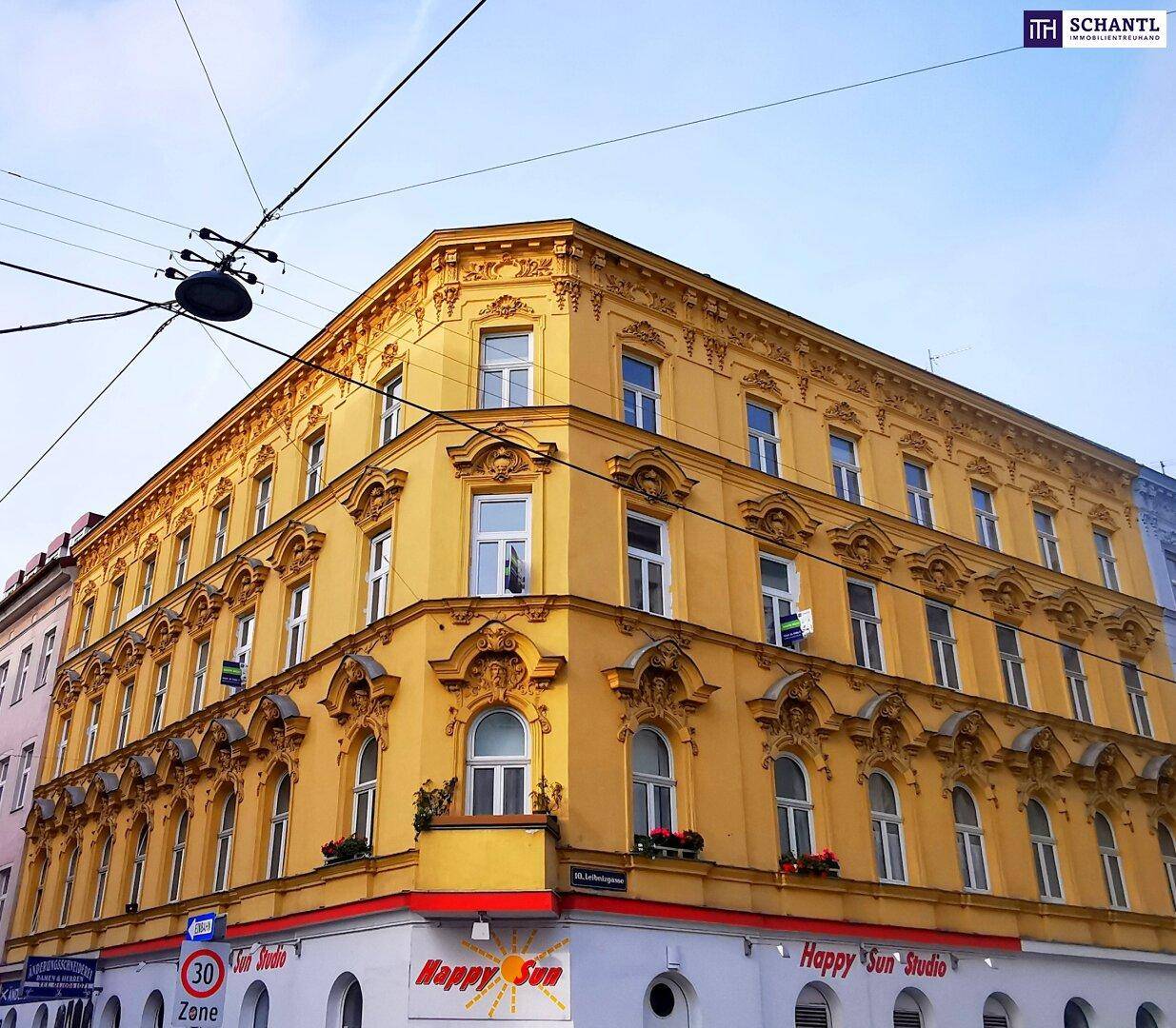Historisches Eckgebäude mit gelber Fassade, reich verzierten Fenstern und Geschäften im Erdgeschoss.
