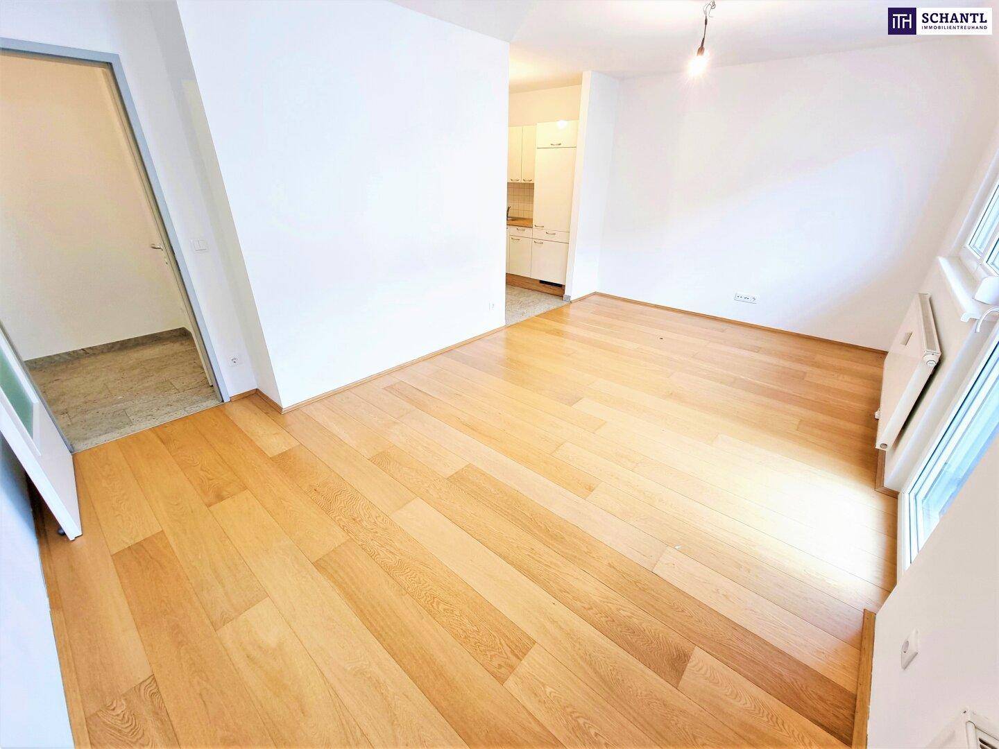 Heller Wohnbereich mit Holzboden und offenem Übergang zur Küche im Hintergrund.