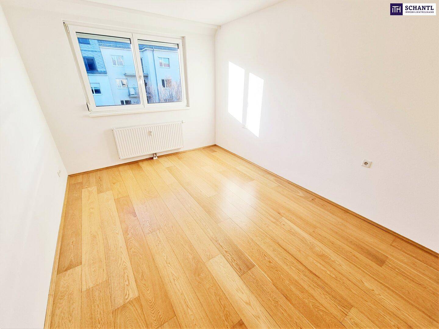 Helles Schlafzimmer mit Holzboden und Fenster, das viel Tageslicht hereinlässt.