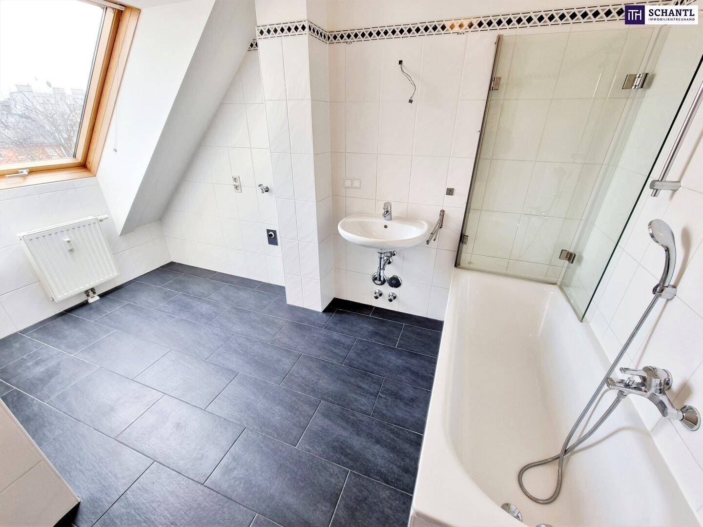 Badezimmer mit weißen Fliesen, dunklem Boden, Badewanne mit Duschwand und Dachfenster.