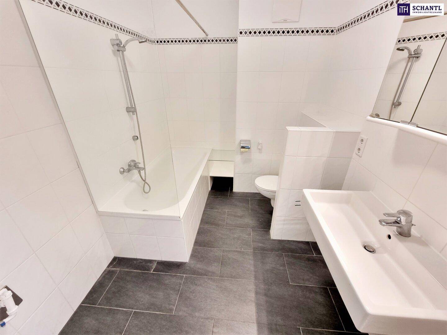 Modernes Badezimmer mit weißen Wandfliesen, dunklem Boden, Badewanne und Waschbecken.