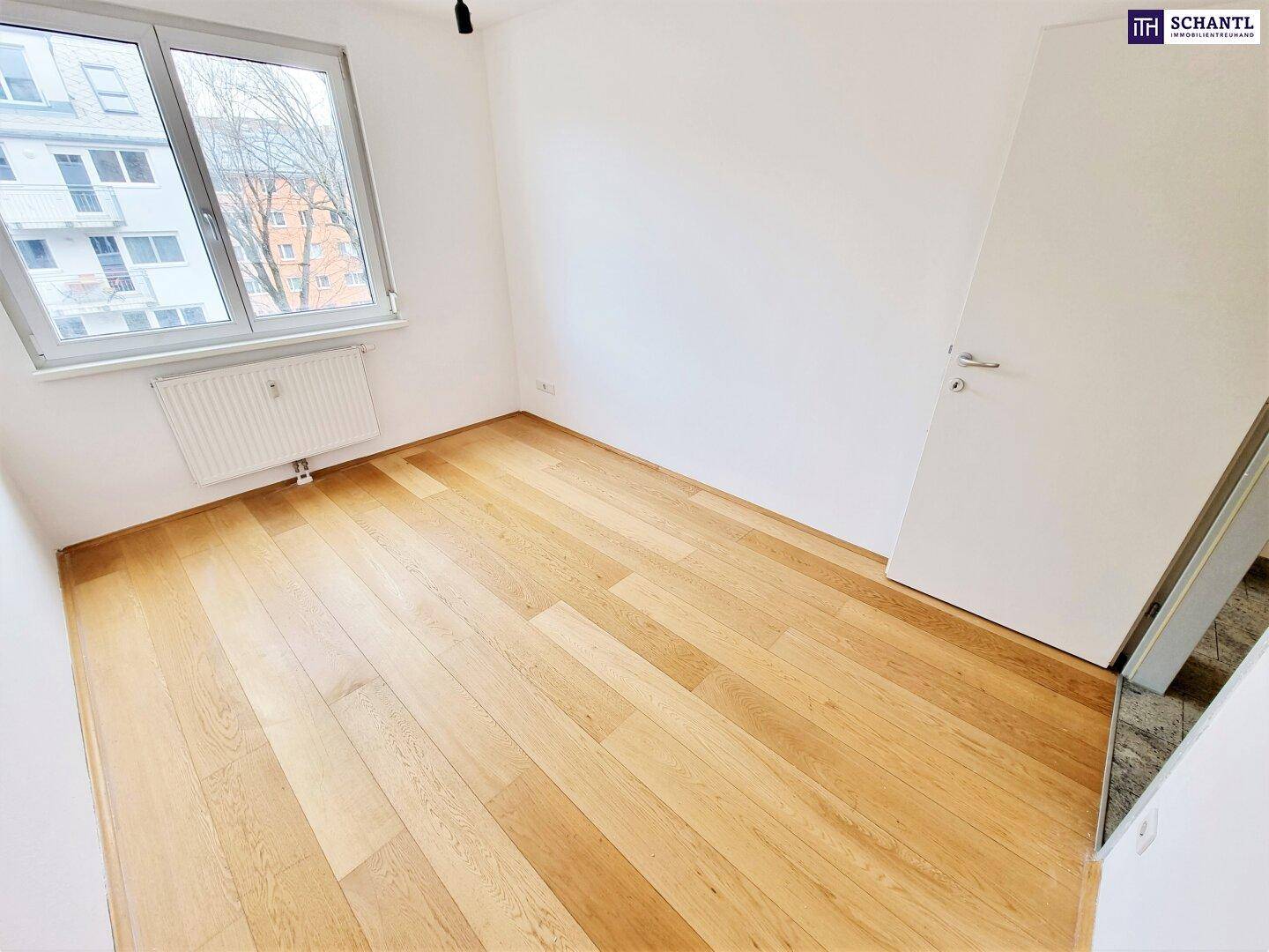 Helles Zimmer mit Holzboden und Fenster, das einen Blick auf die Umgebung bietet.
