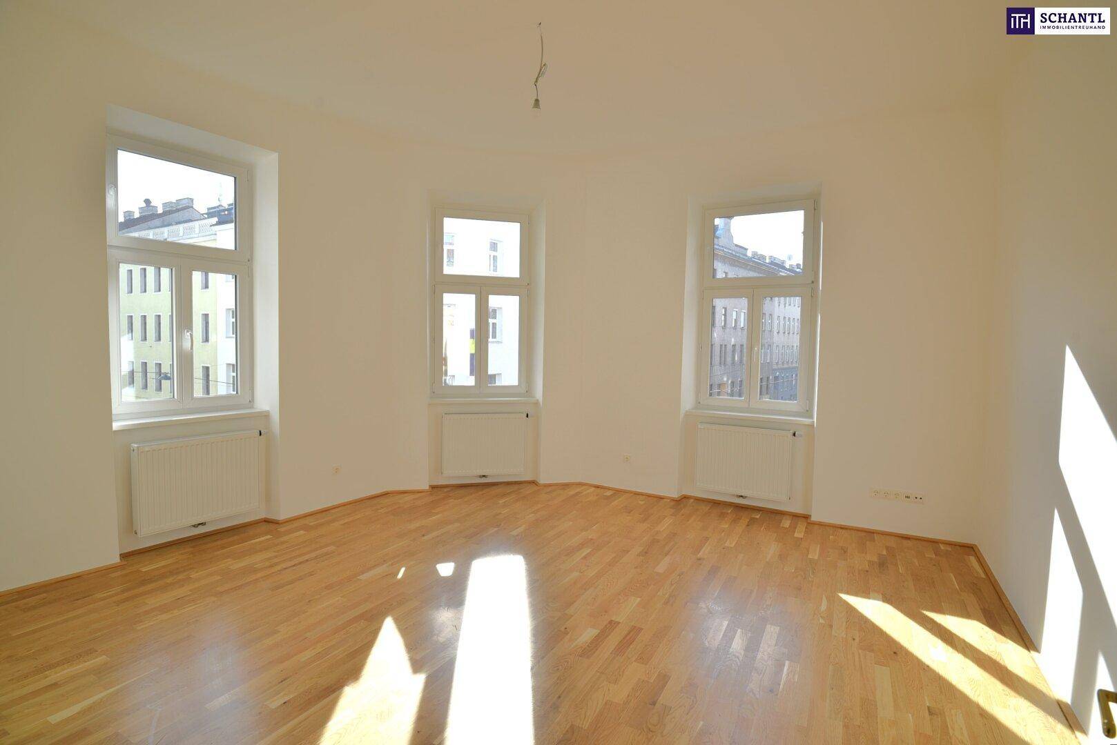 Heller, leerer Raum mit Holzboden und mehreren Fenstern, ideal als Wohnzimmer.