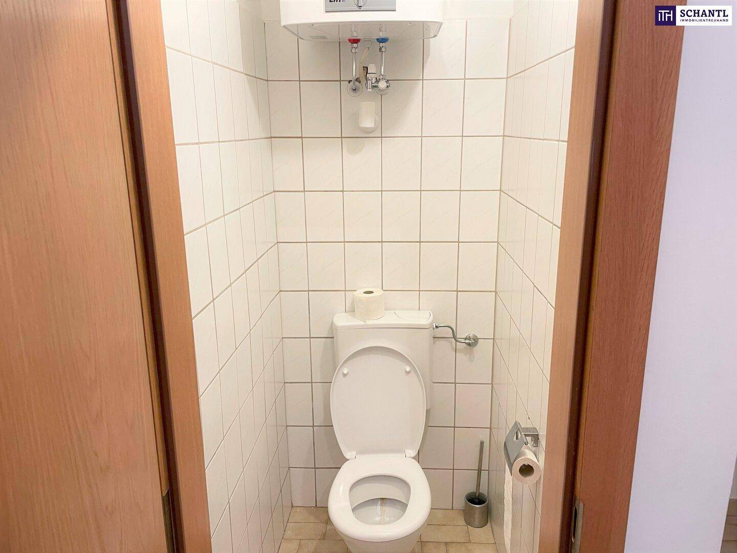 Kleines, gefliestes WC mit Toilette und Warmwasserboiler an der Wand.