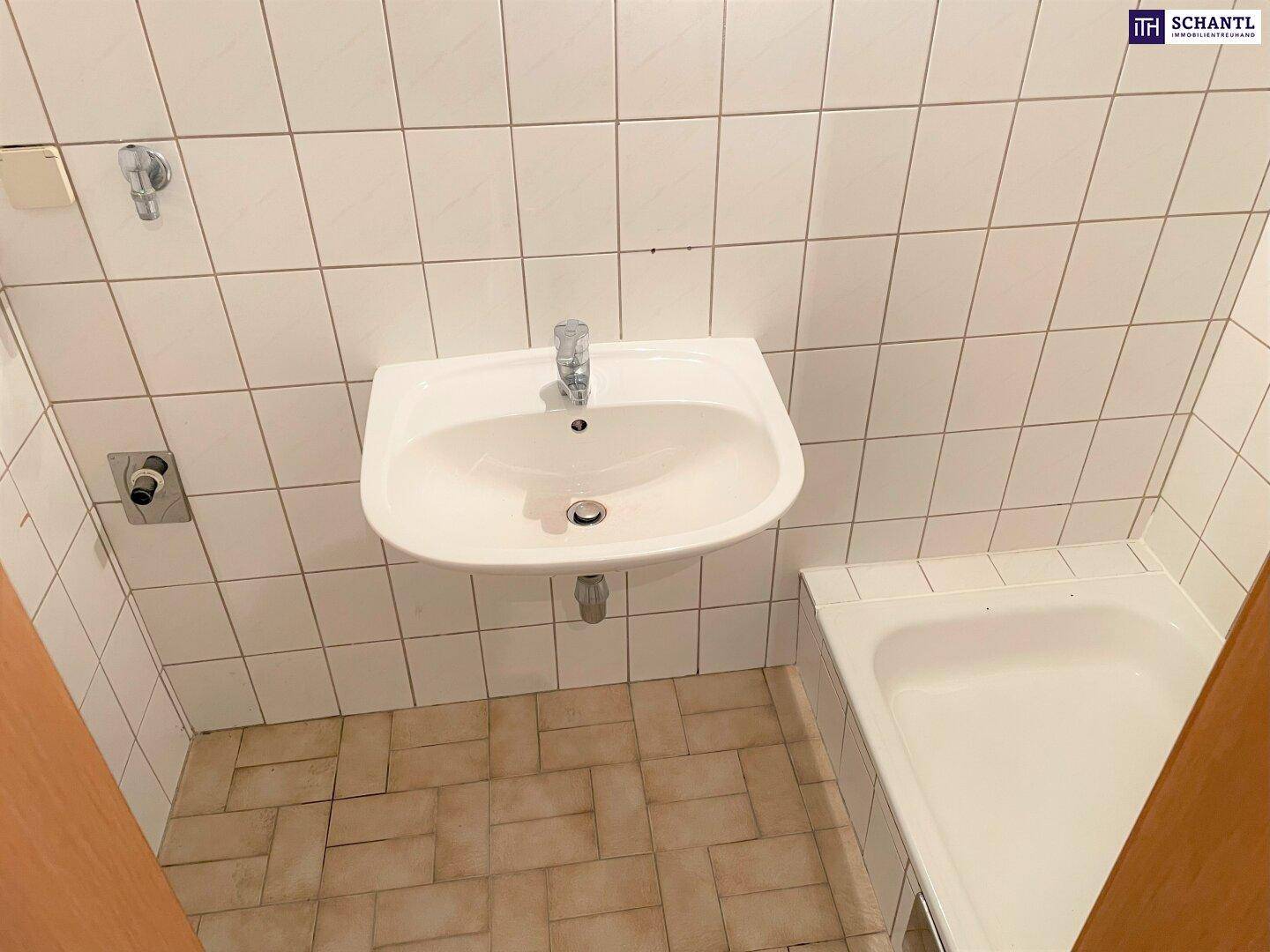 Badezimmer mit weißen Wandfliesen, einem Waschbecken und einer kleinen Badewanne.