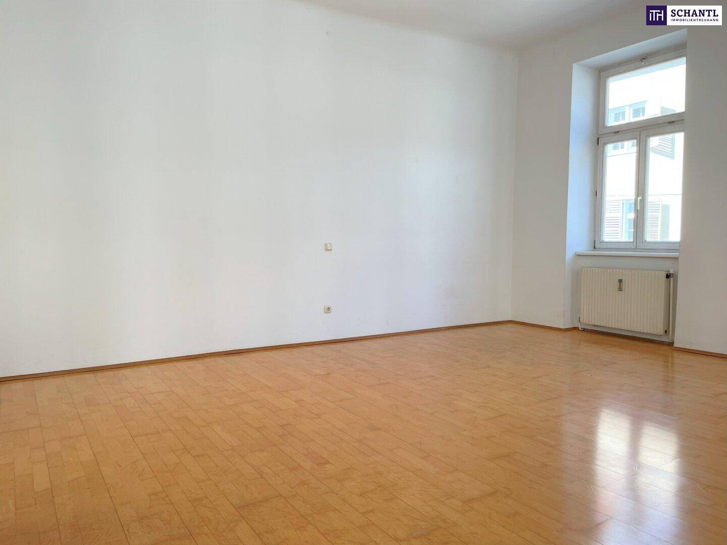 Geräumiges Zimmer mit hellem Parkettboden, weißen Wänden und einem großen Fenster.